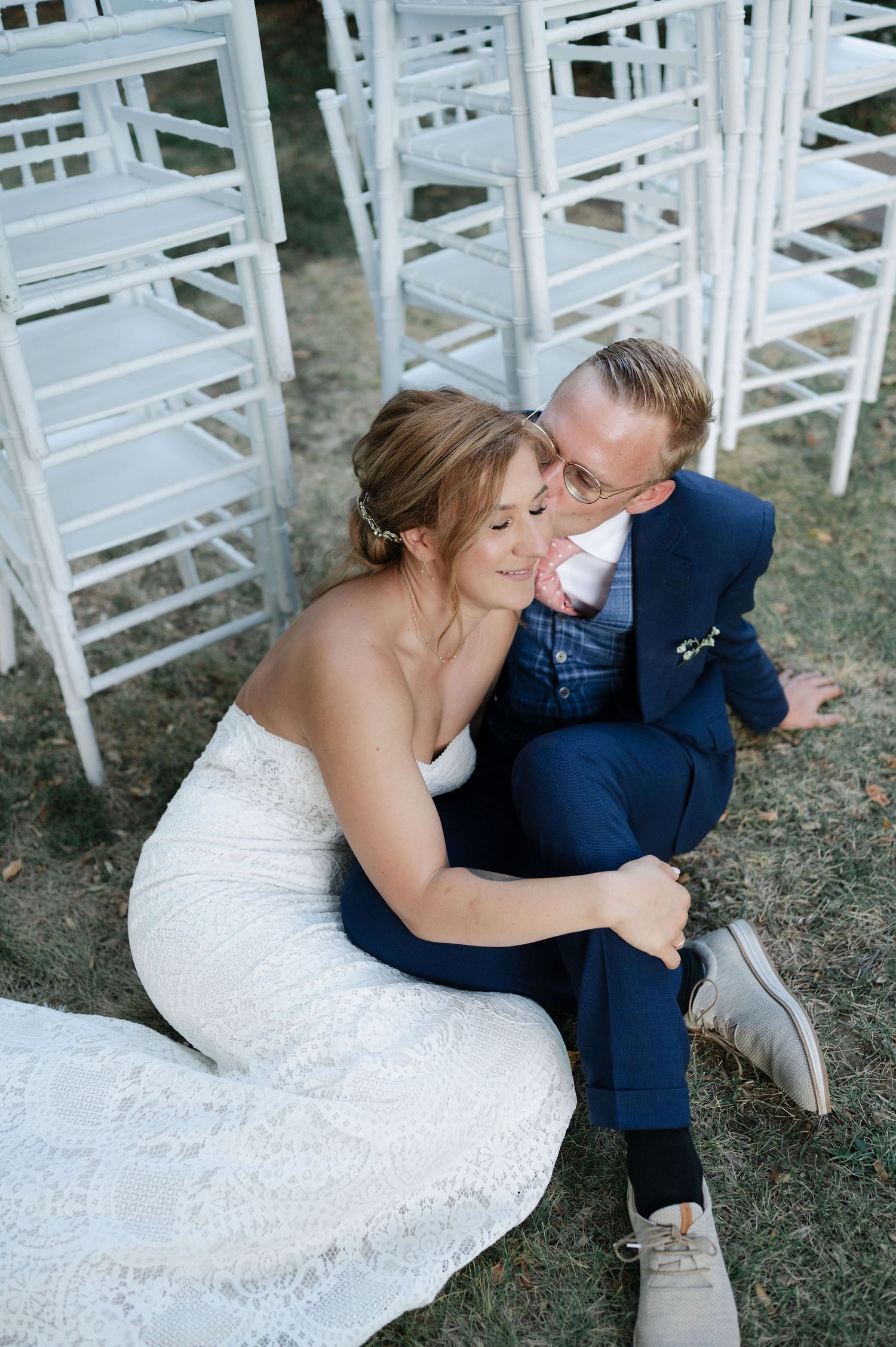 A romantic moment between newlyweds sitting among white garden chairs.