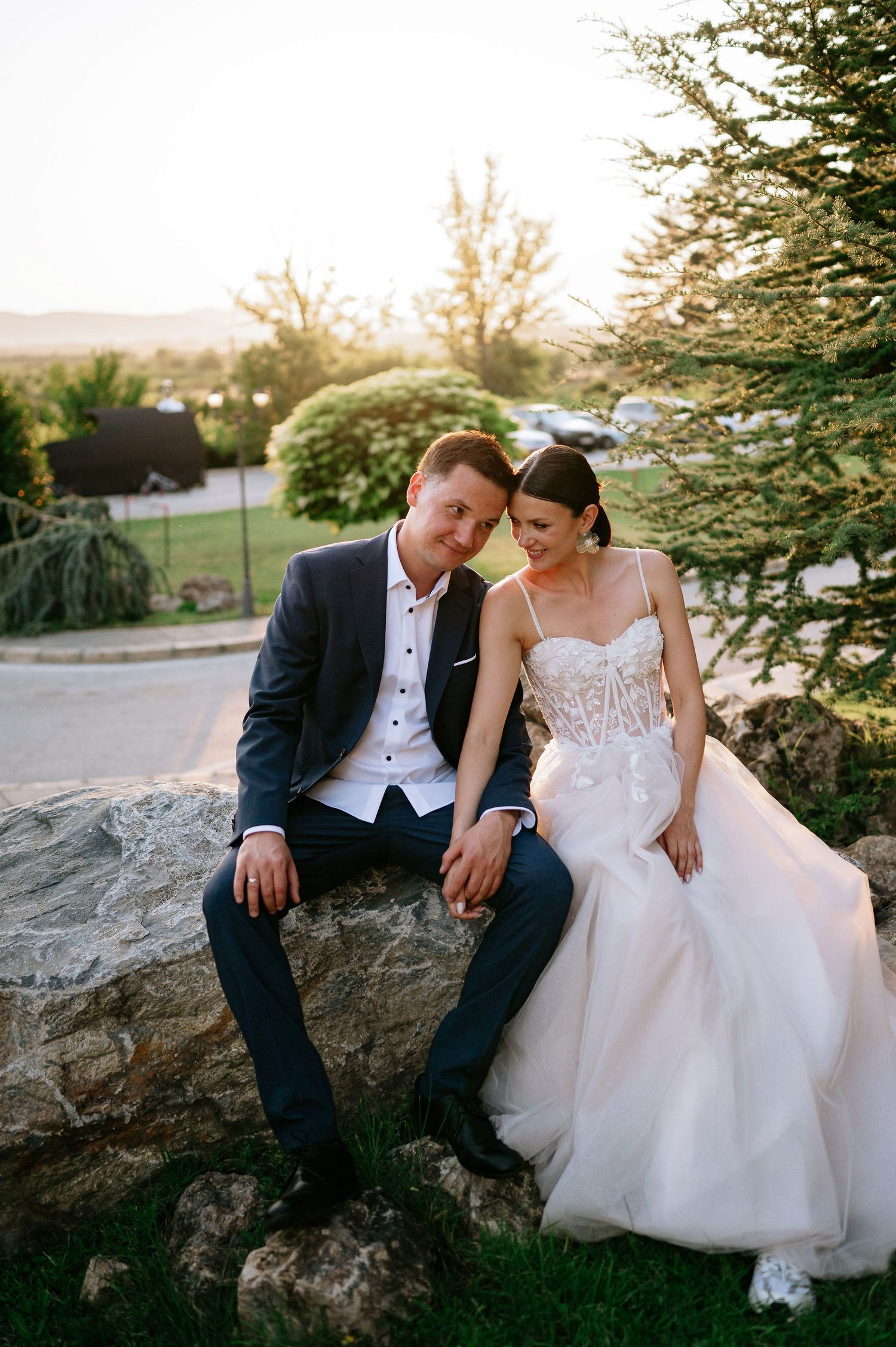 Couple in wedding attire sharing quiet moments on a large rock at sunset.