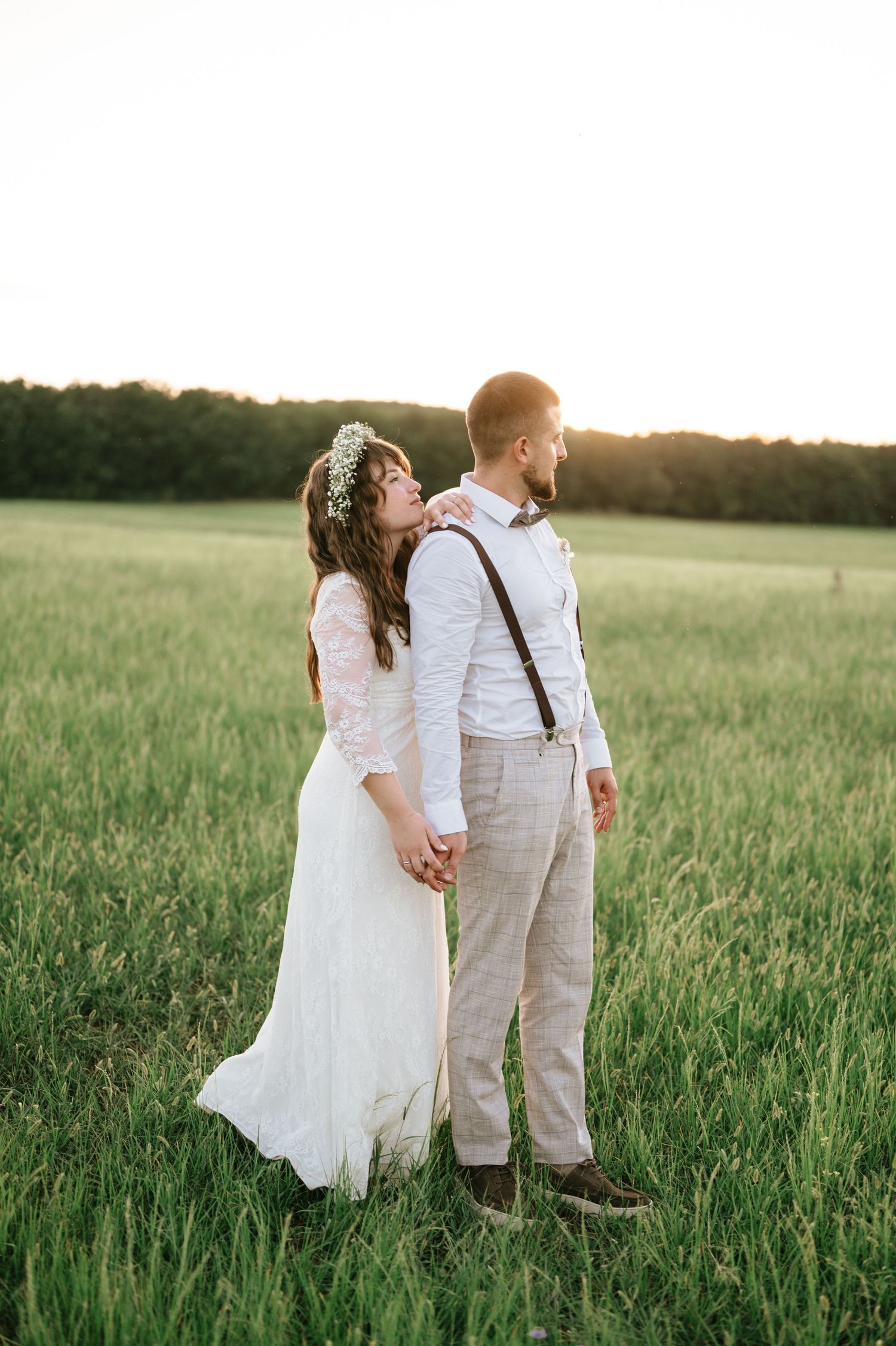 A couple holds hands while walking through a scenic field at sunset.
