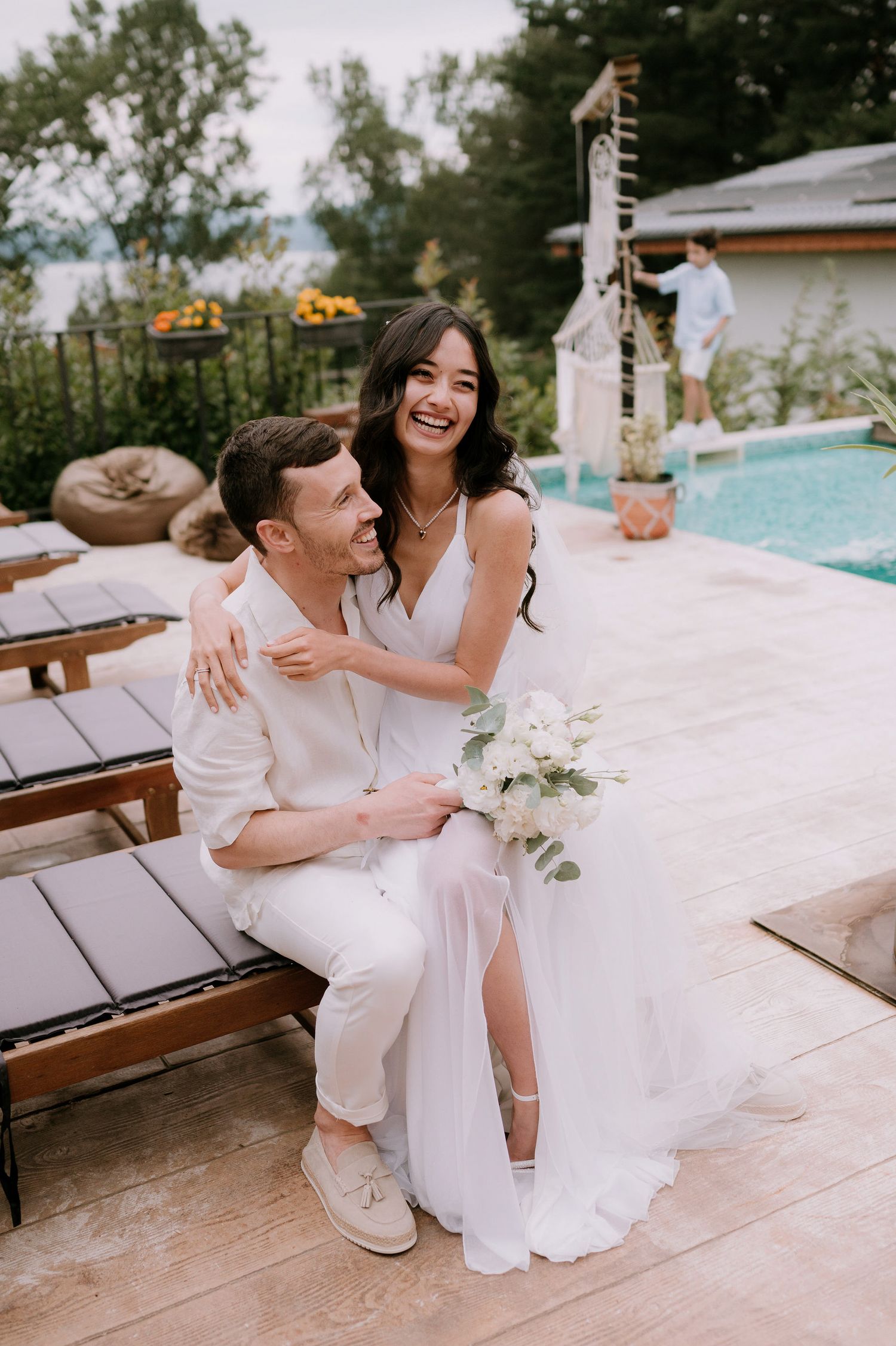 Joyful wedding couple shares laughs and embraces during poolside photo session.