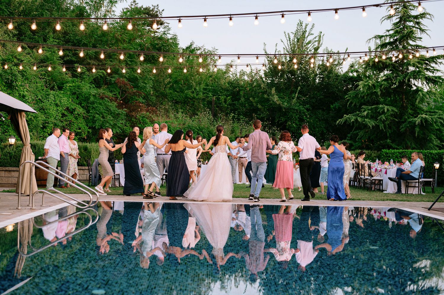People dancing and celebrating under string lights at an outdoor evening event.