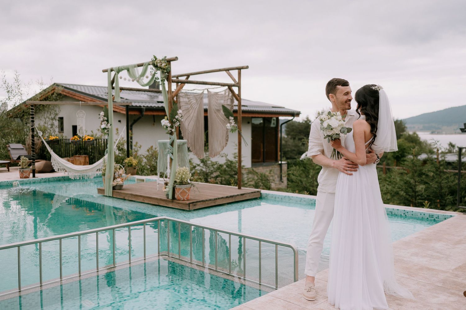Romantic wedding ceremony setting with wooden pergola and pool deck in mountain surroundings.