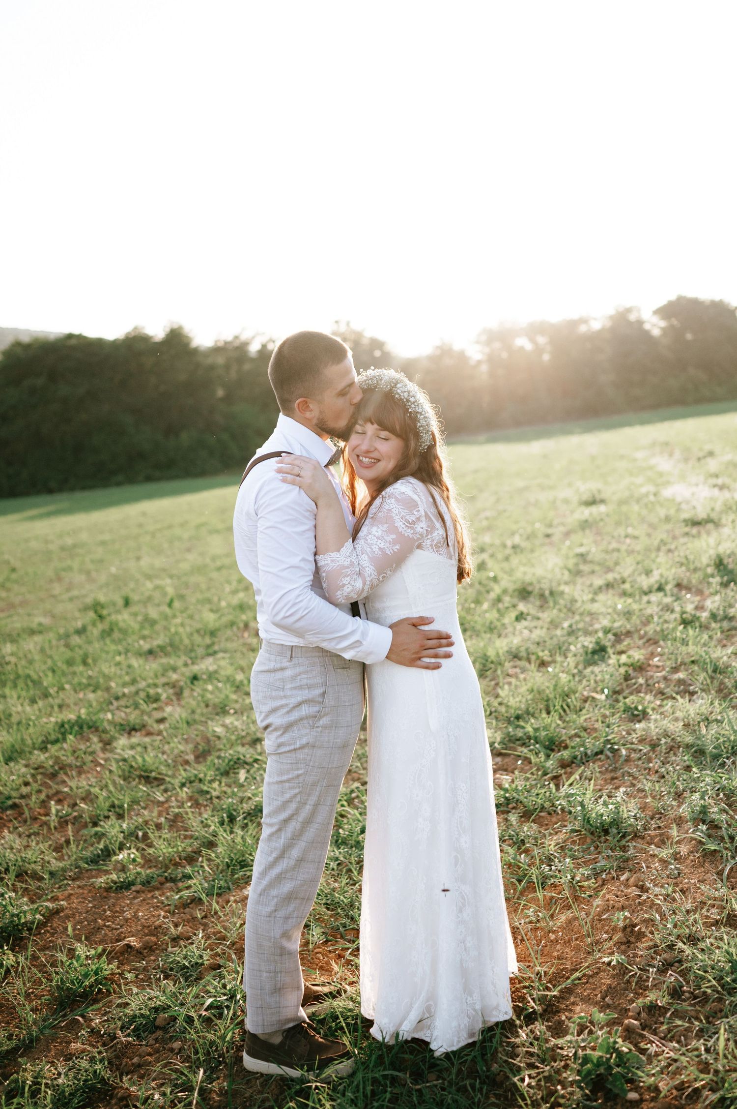 A tender wedding moment captured in a sun-drenched field during golden hour.