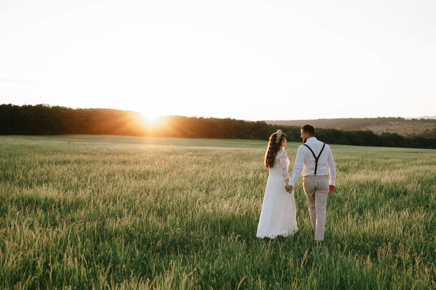 A scenic sunset view over rolling green fields with silhouettes in the distance.