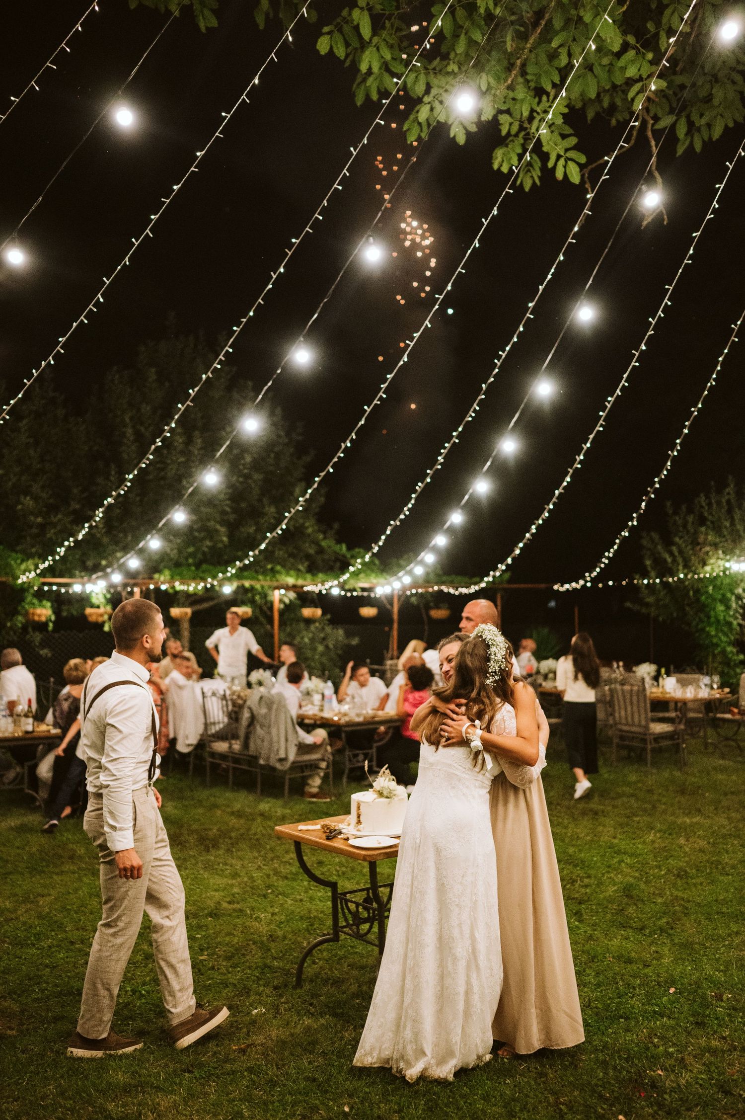 Evening wedding reception with twinkling lights strung above guests mingling outdoors.