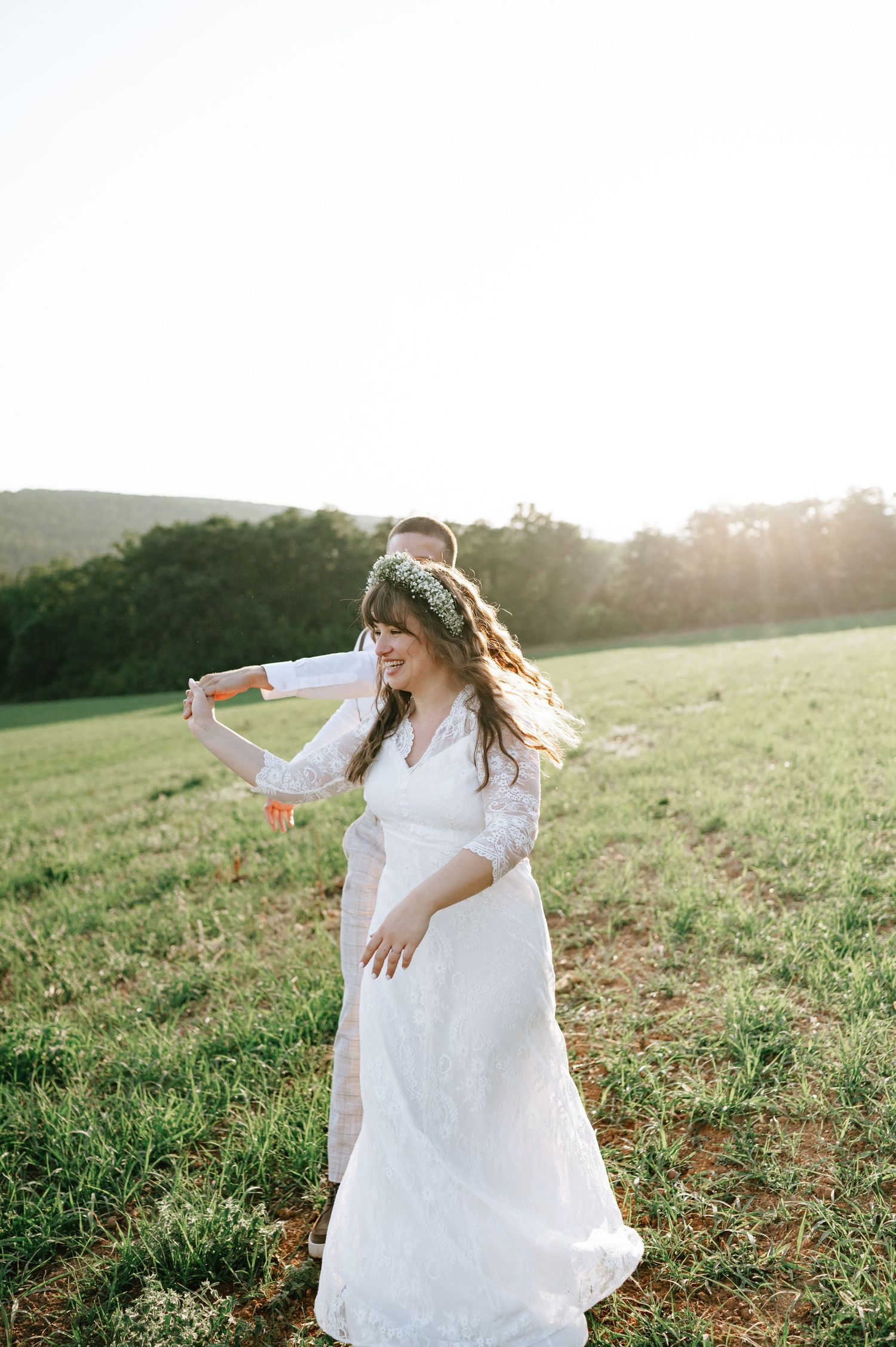 A bride spins gracefully in a white lace dress against a sunset meadow backdrop.