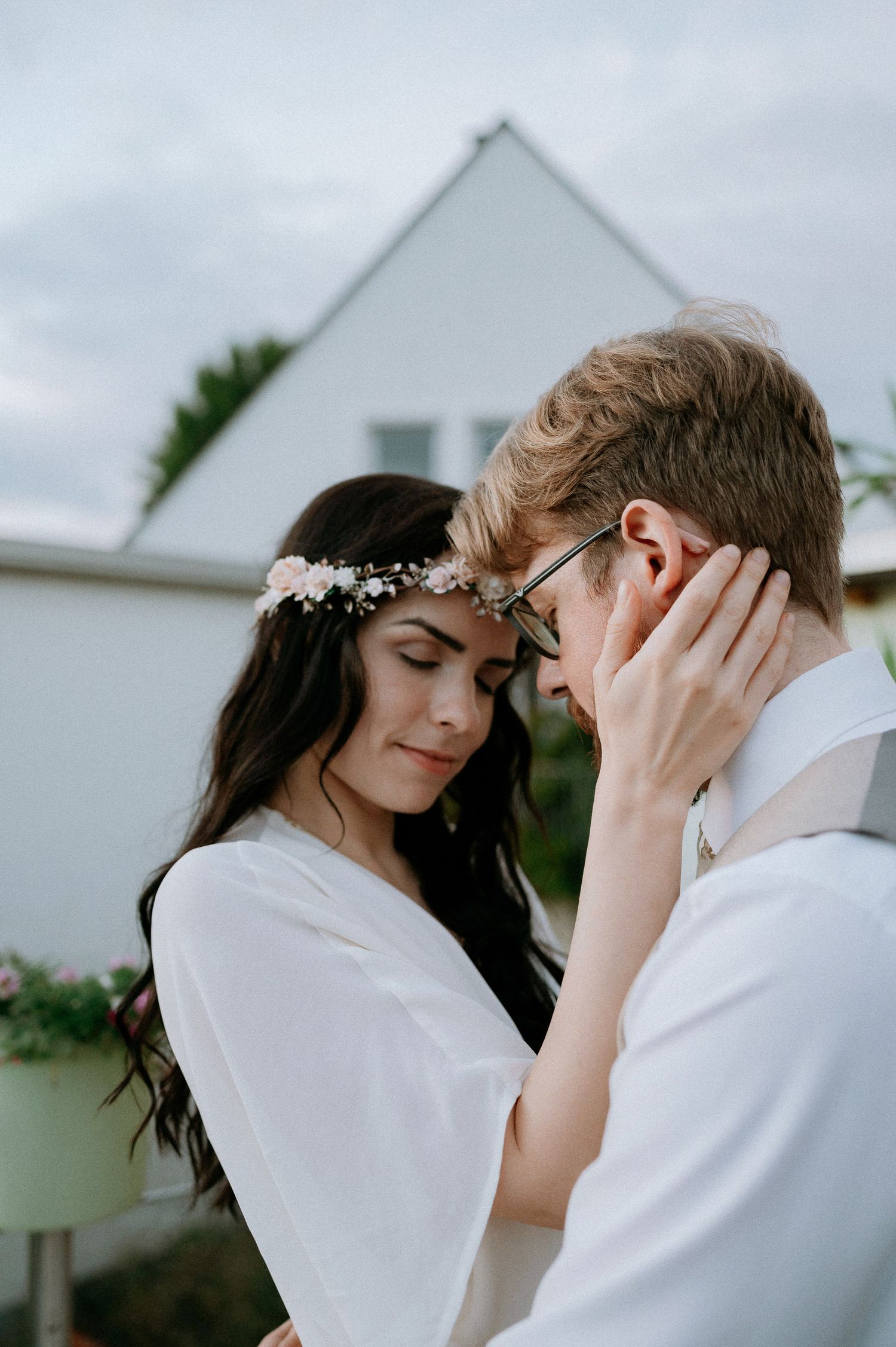 A tender forehead touch between newlyweds against a white house backdrop.
