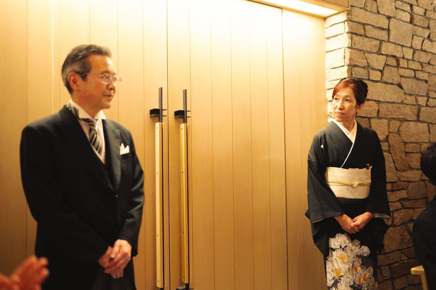 Guests in traditional formal wear stand in a warmly lit hallway with stone accents.