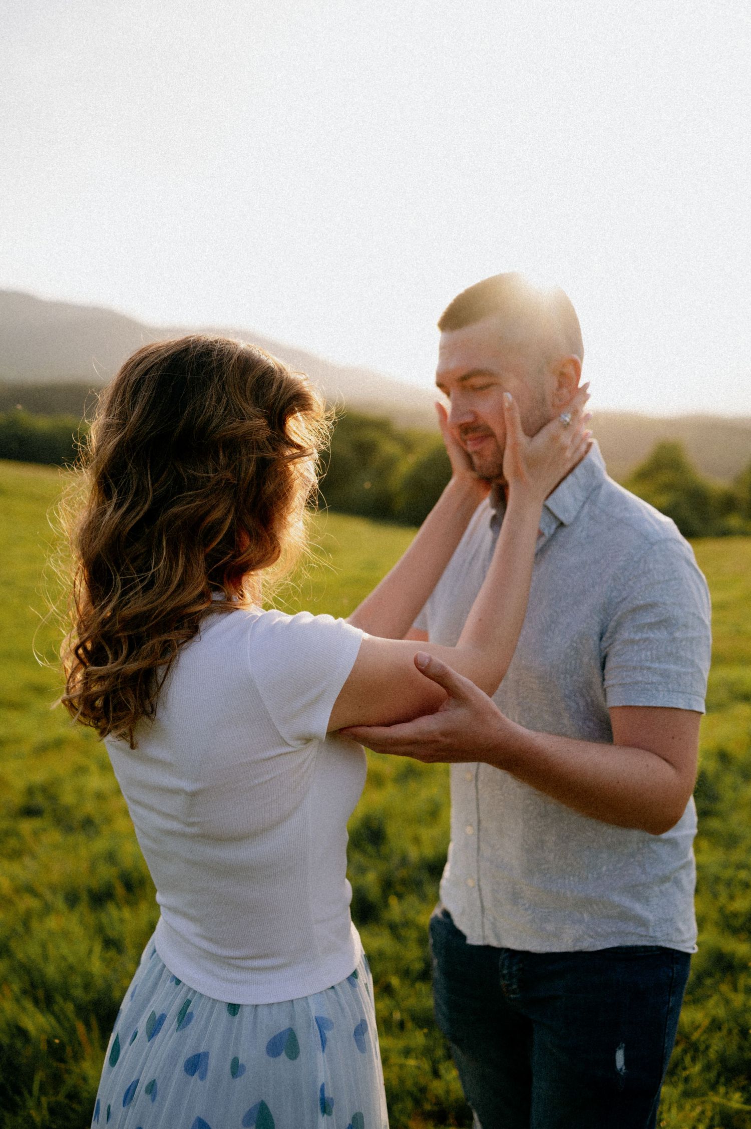 A couple shares a playful moment in a sun-drenched field.