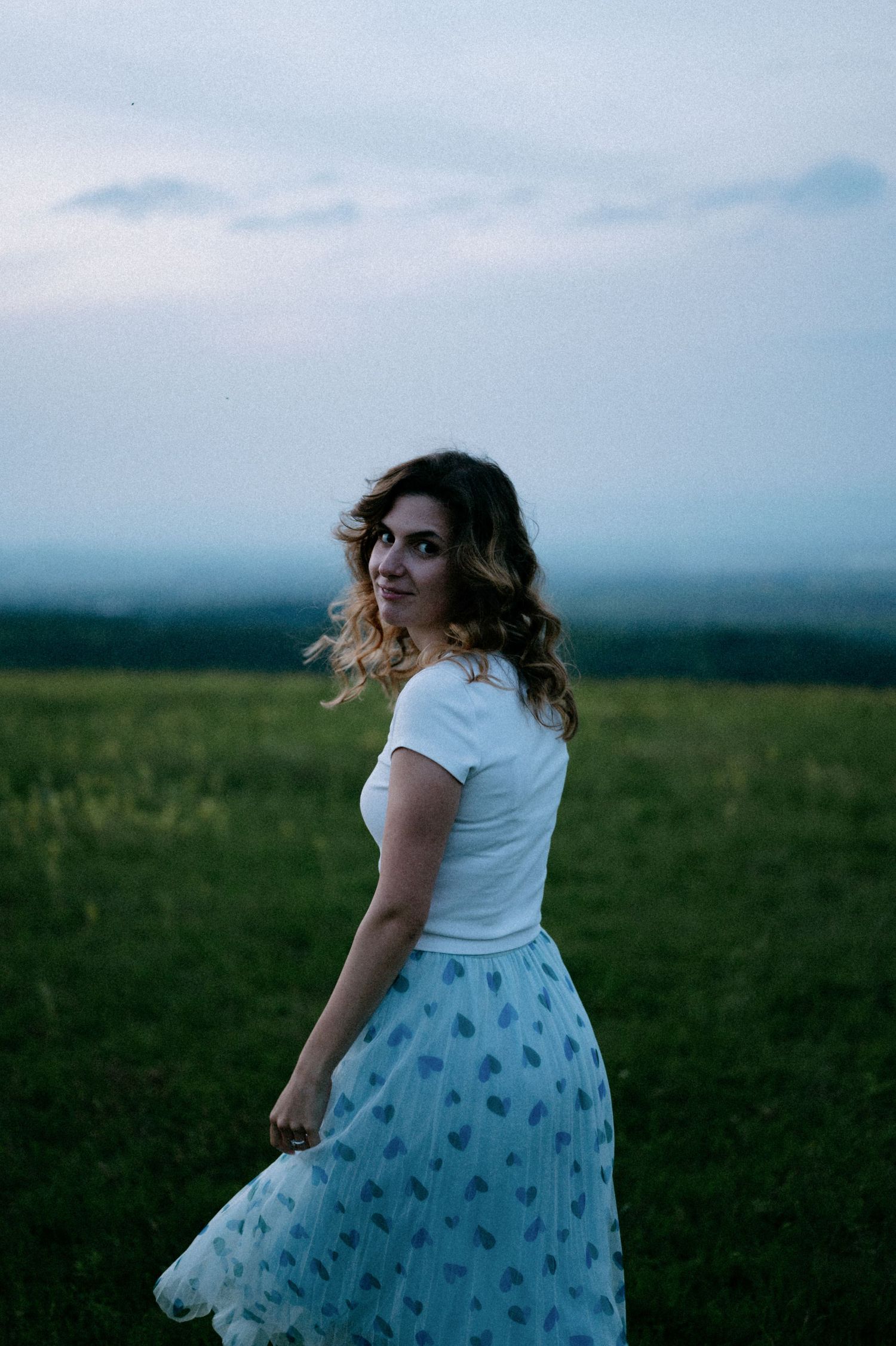 A person in summer attire twirls on a hilltop during golden hour.