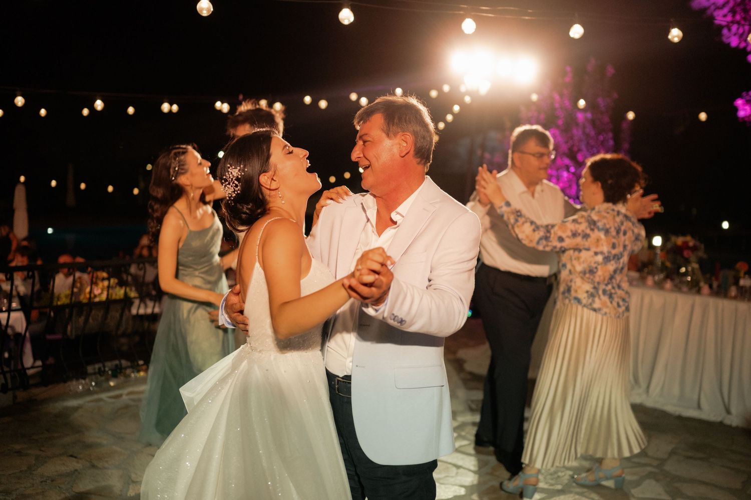 Couples dancing together at an evening wedding reception with string lights glowing overhead.