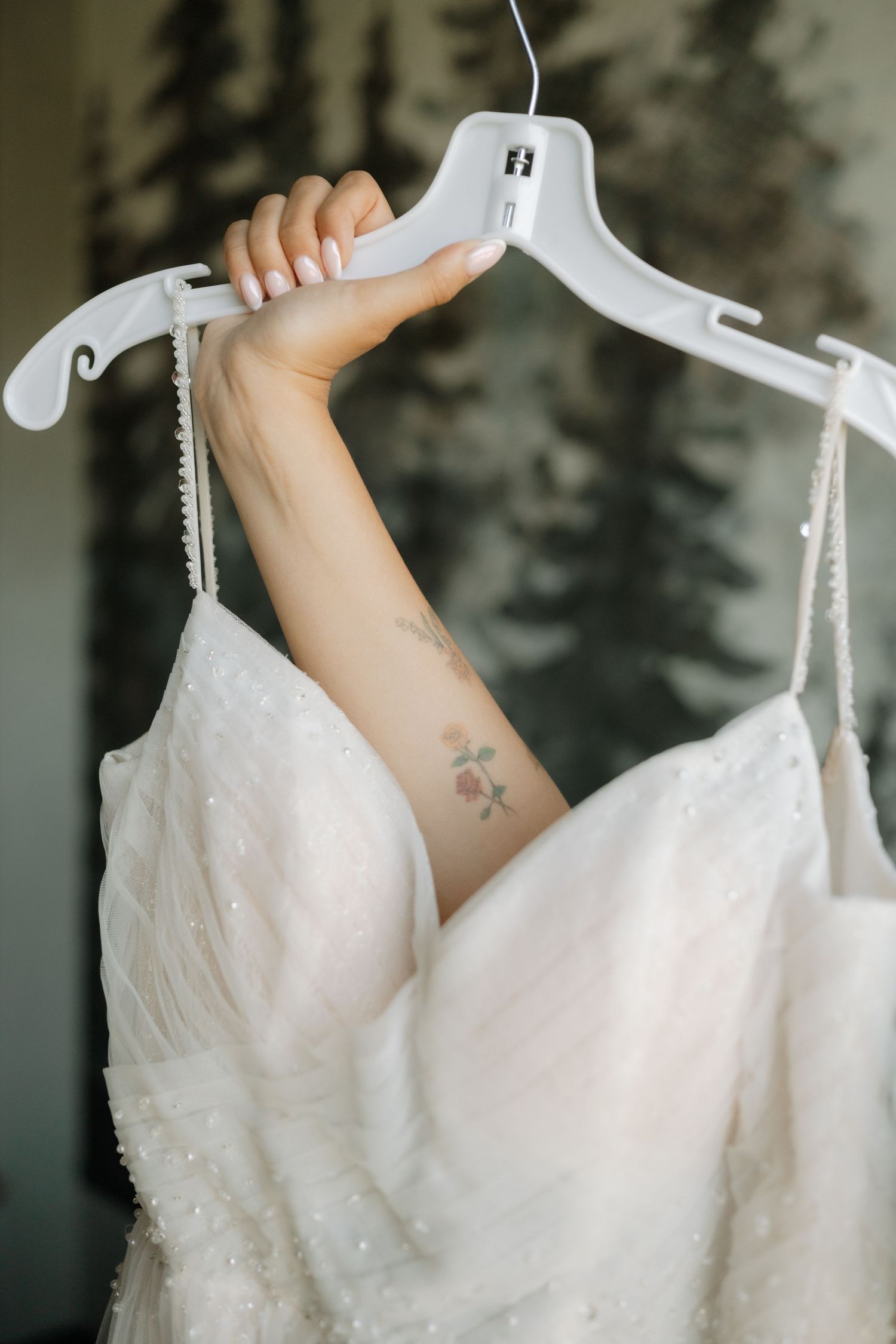 Close-up sequence of hands lifting a white beaded wedding dress on a hanger against a blurred background.