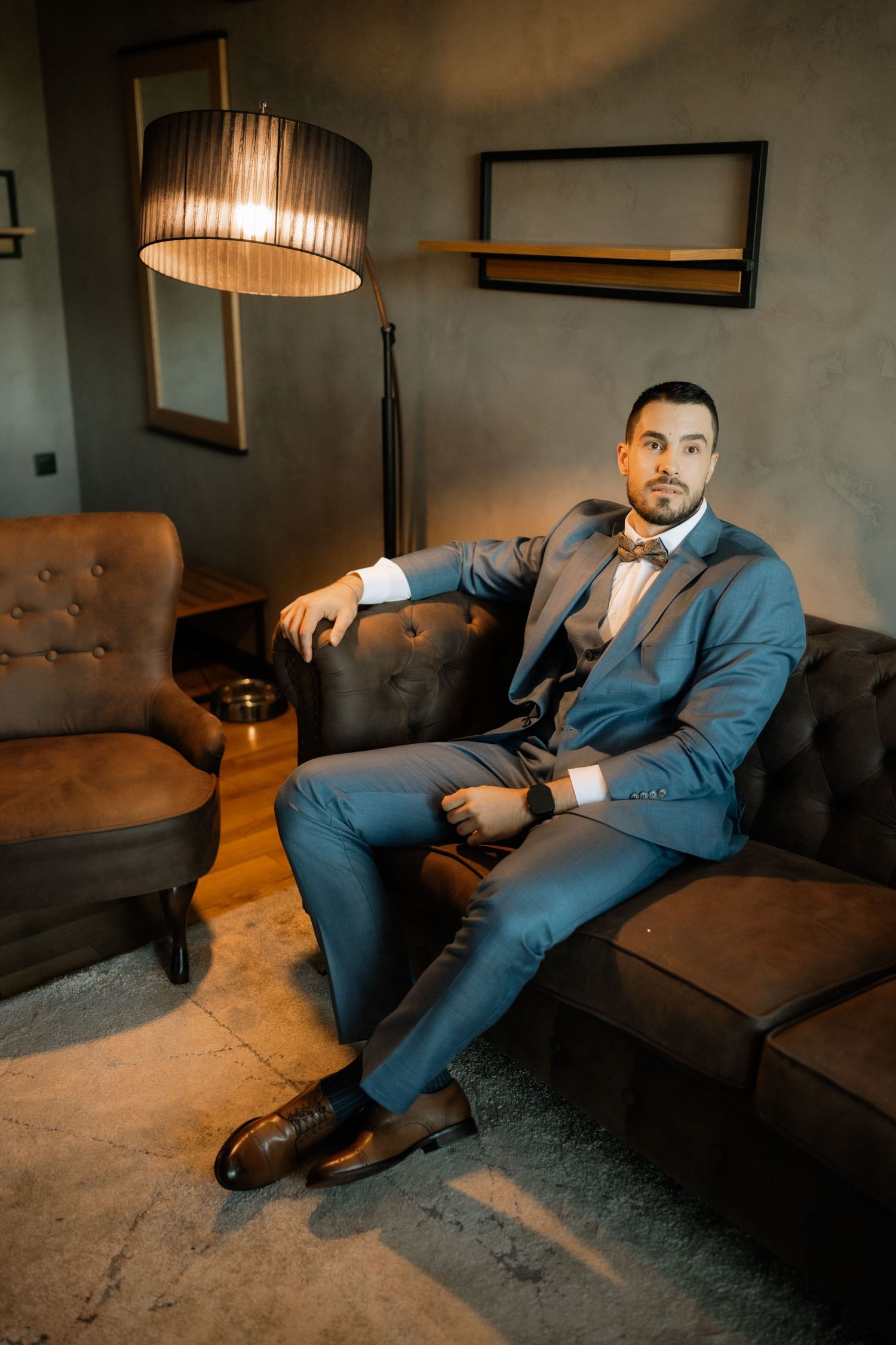 Professional portrait series showing a person in a blue suit lounging on a leather couch in moody lighting.