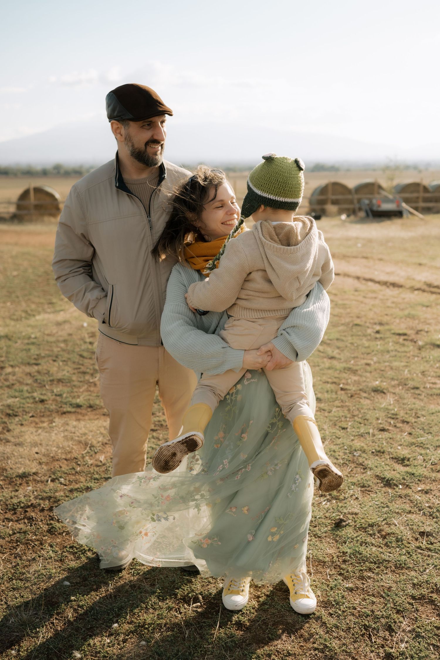 Family in neutral colored clothing plays together in a grassy field during golden hour.