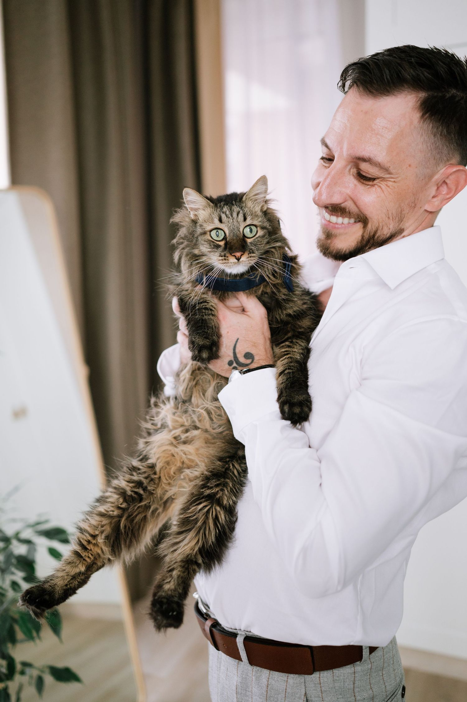 A fluffy brown cat with wide eyes being held up in the air by someone wearing a white shirt.