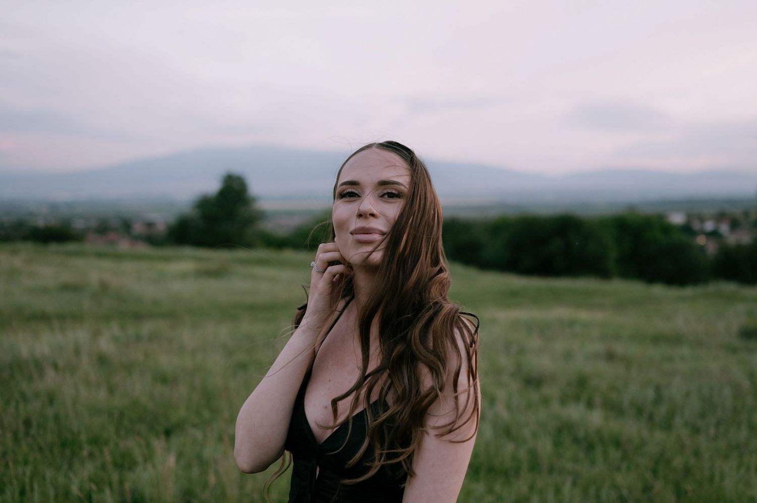 A person stands in a lush green meadow at sunset with mountains visible in the background.