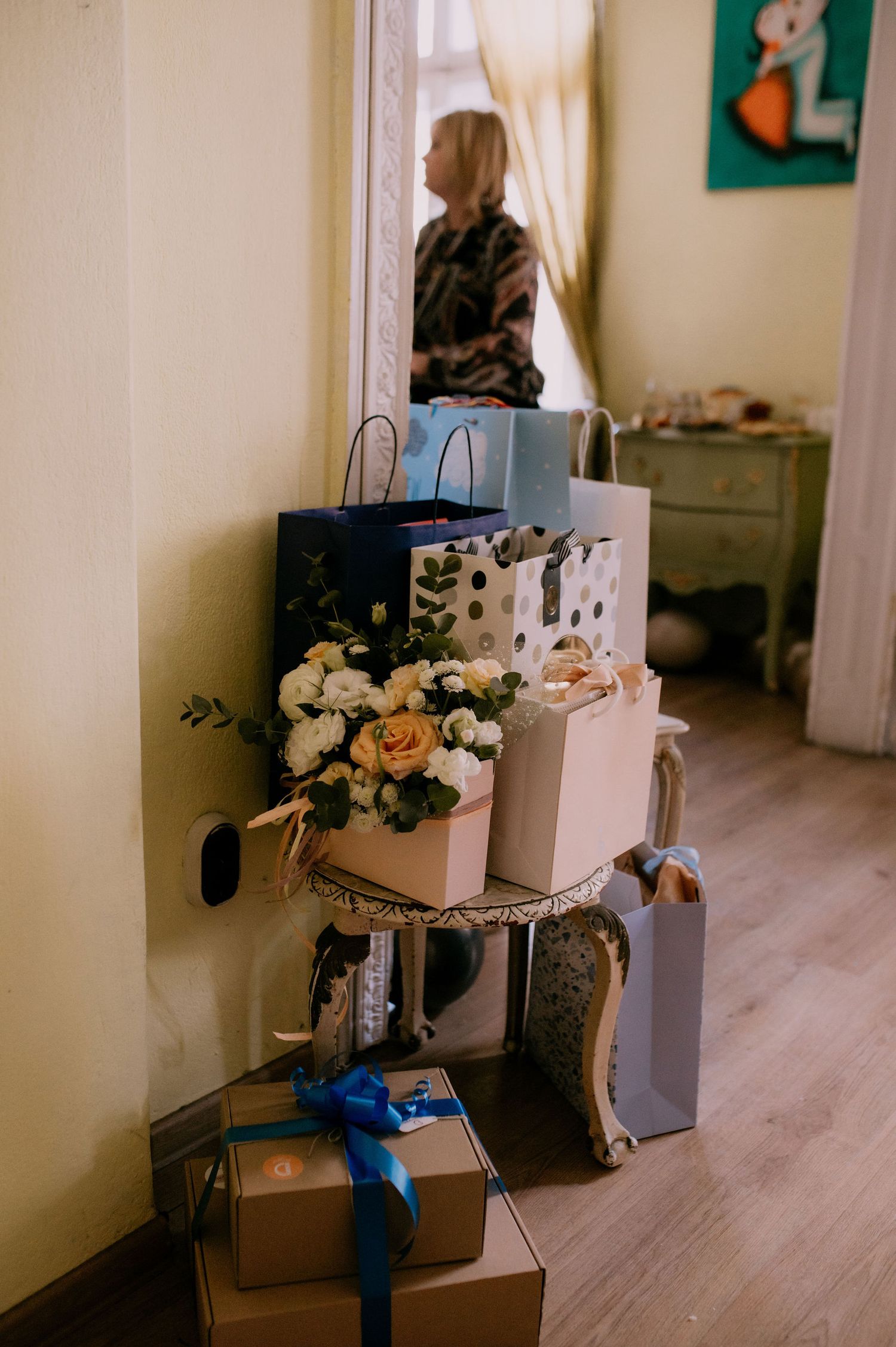 A series of four similar photos showing a white box with flowers and blue ribbon sitting on a wooden floor.