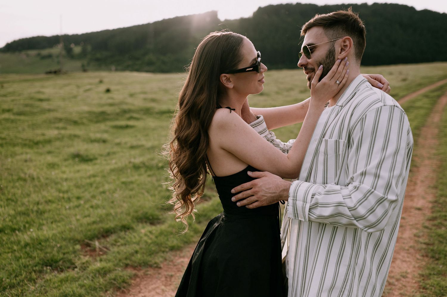 A couple shares romantic moments together on a scenic hillside path during golden hour.