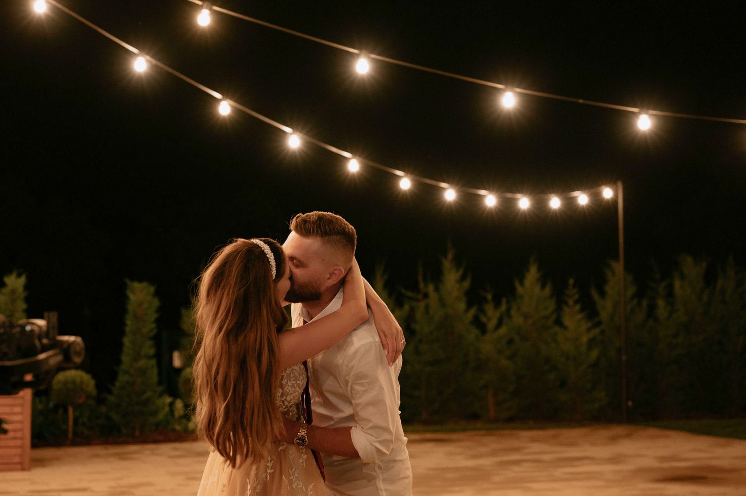 String lights illuminate a romantic outdoor dance scene at dusk with couples swaying together.