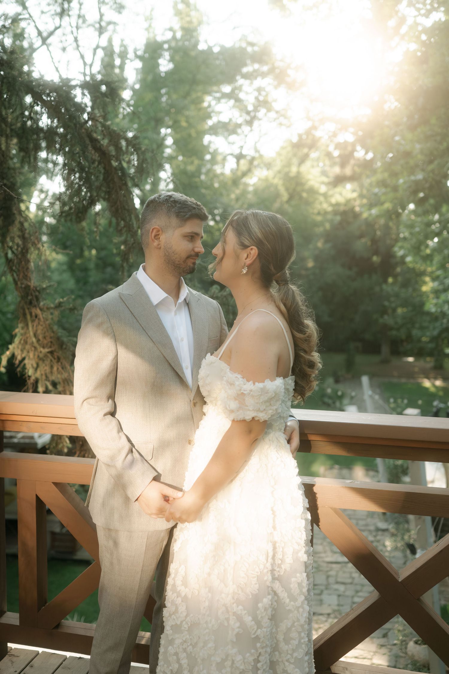 Romantic couple in wedding attire sharing intimate moments on a wooden deck during golden hour sunset.