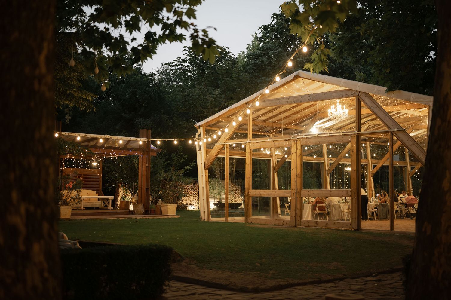 Illuminated outdoor wedding pavilion with string lights glowing at dusk in a rustic setting.