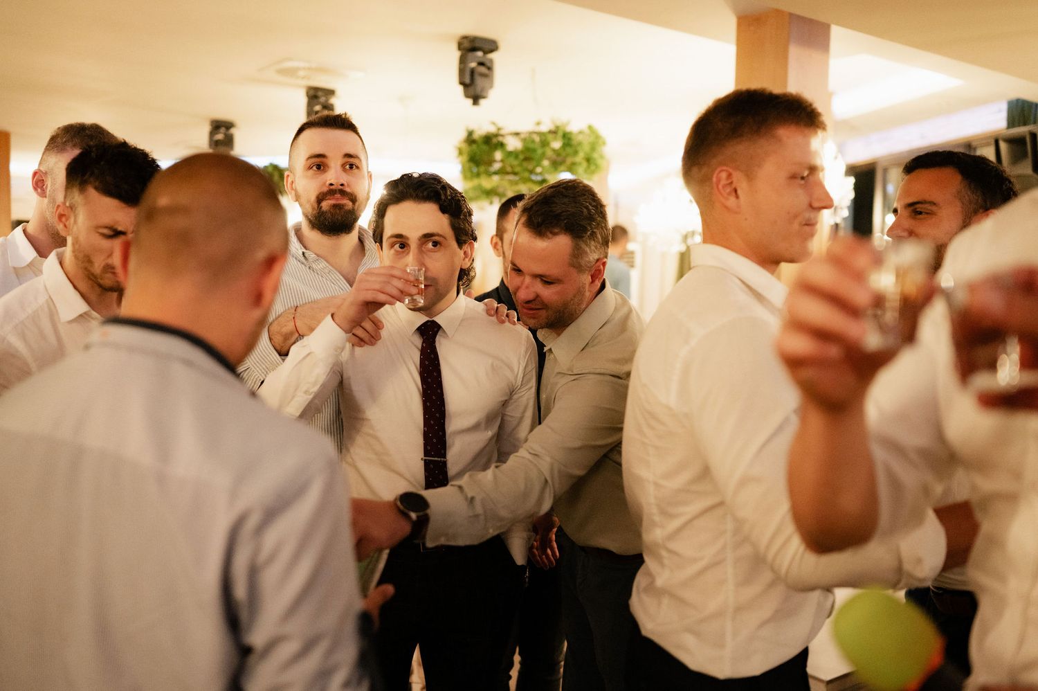 A group of wedding guests raise their glasses in a celebratory toast during a reception.