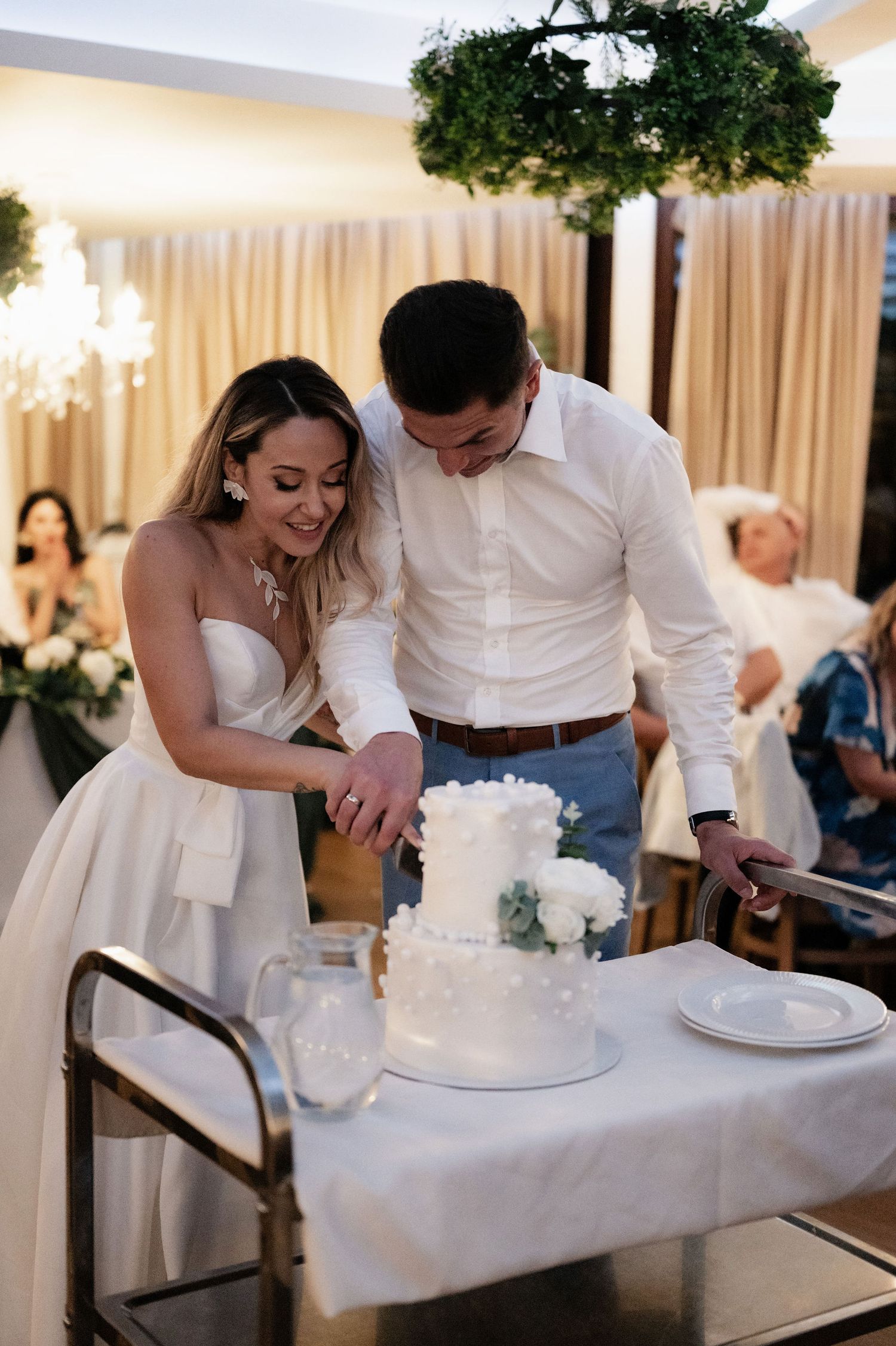 Couple cutting into their white wedding cake together during reception celebration.