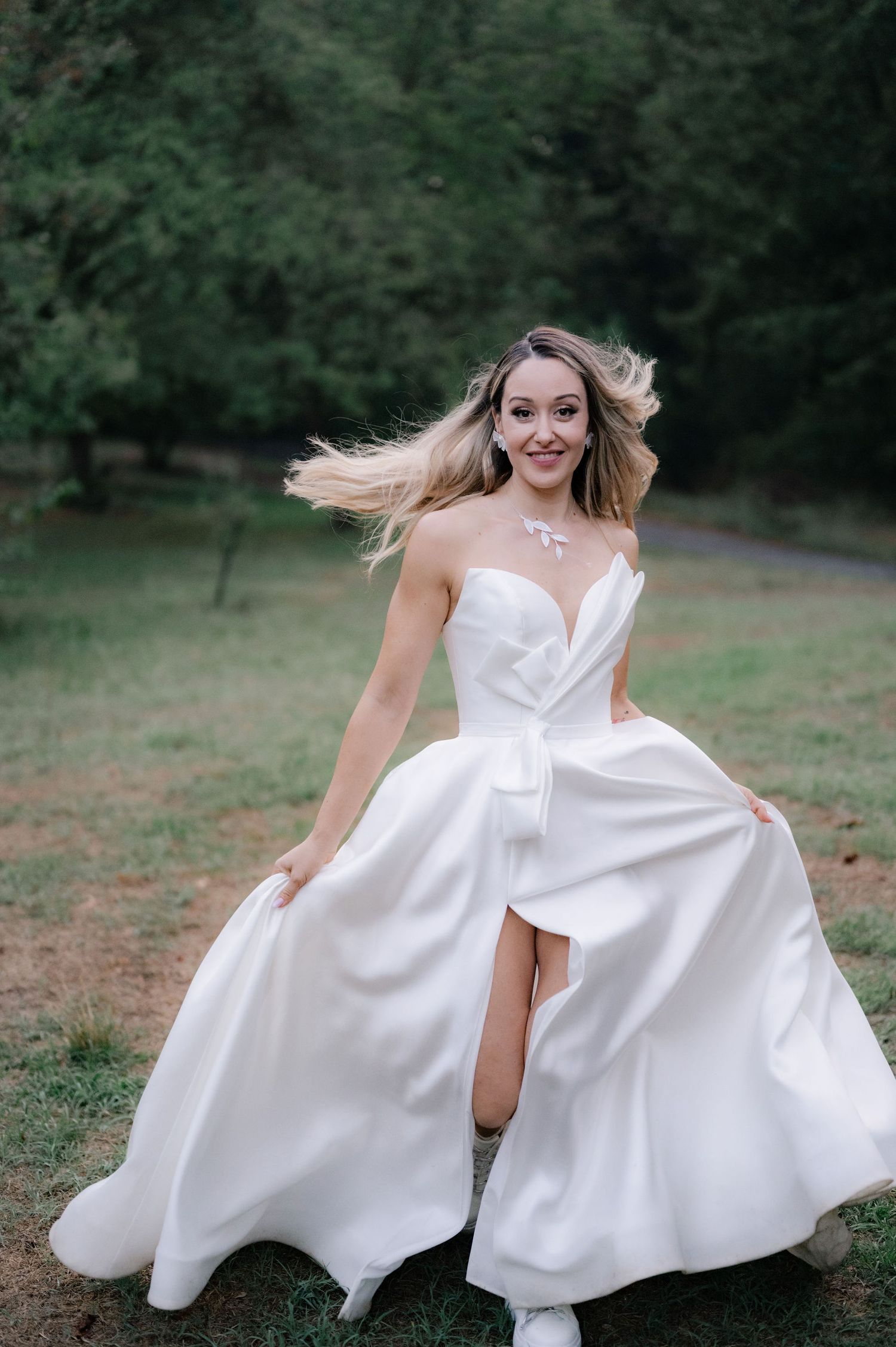 A flowing white wedding dress twirls gracefully in an outdoor garden setting with trees in the background.
