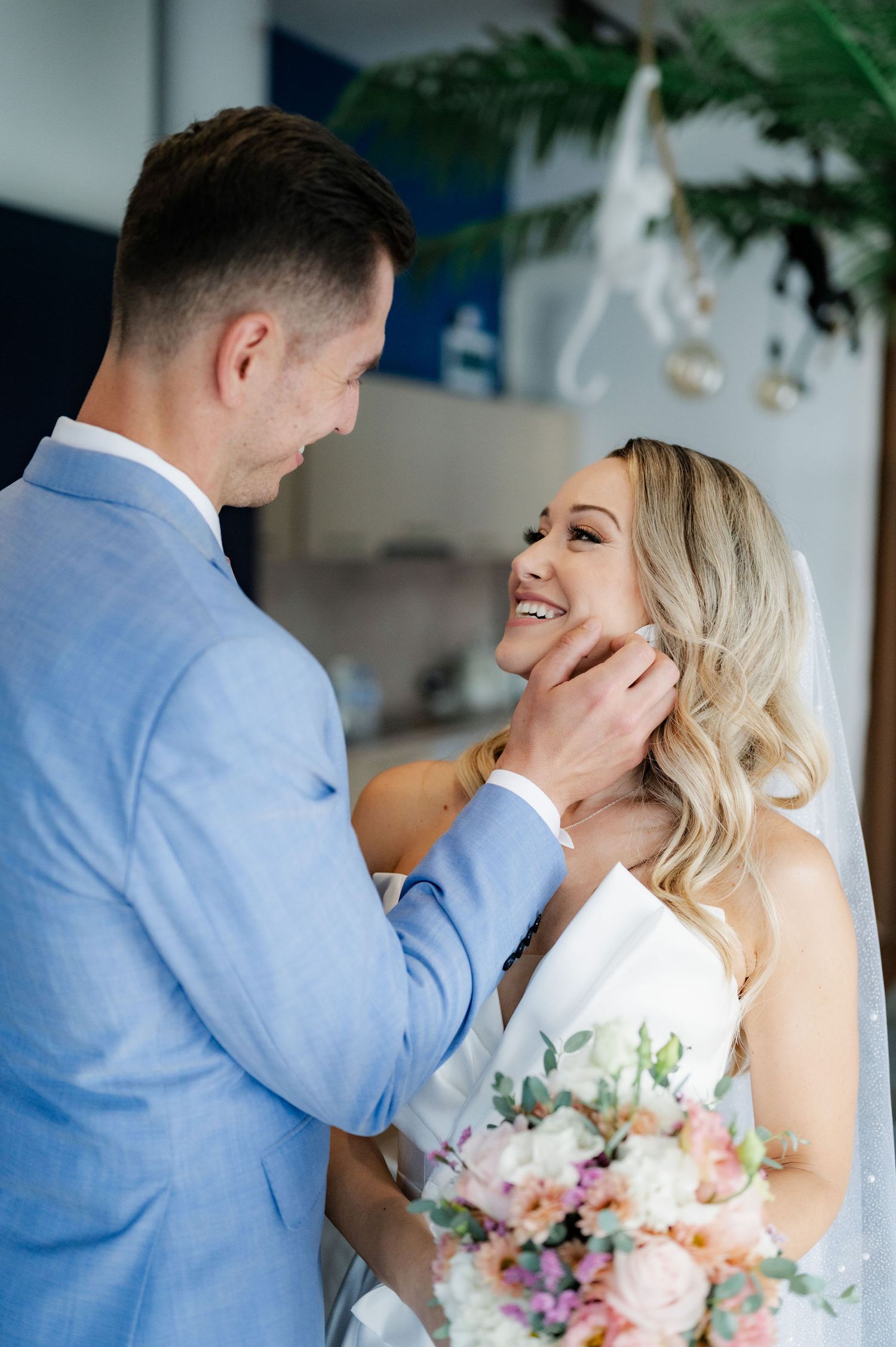 A tender moment between newlyweds as they share an intimate gesture while holding a pastel floral bouquet.