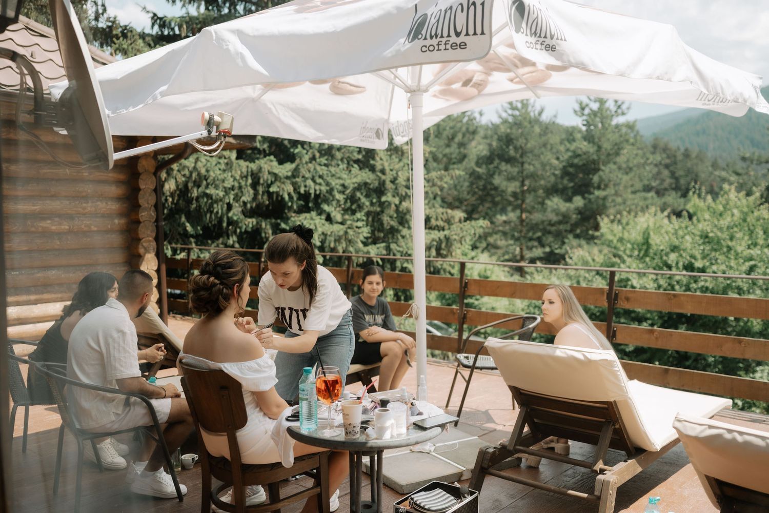 Outdoor restaurant terrace with white umbrellas and wooden furniture overlooking a scenic mountain landscape.