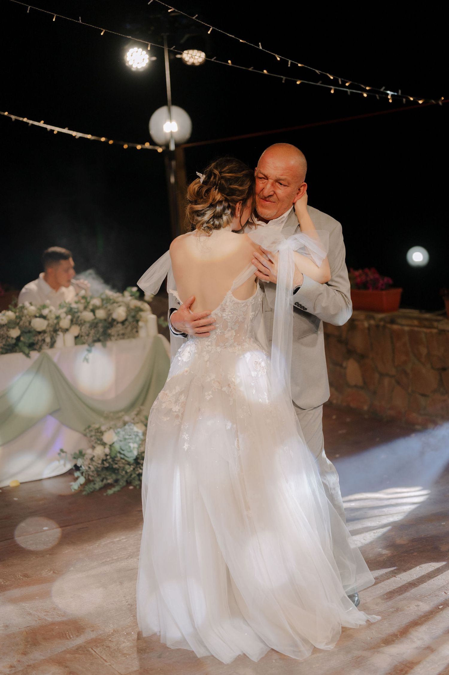 A touching dance sequence between family members at a wedding reception with decorative lighting and floral arrangements.