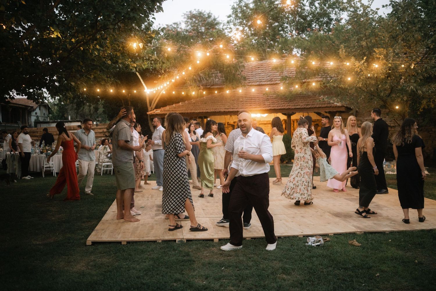 People dancing on an outdoor dance floor under string lights at dusk during a festive outdoor celebration.