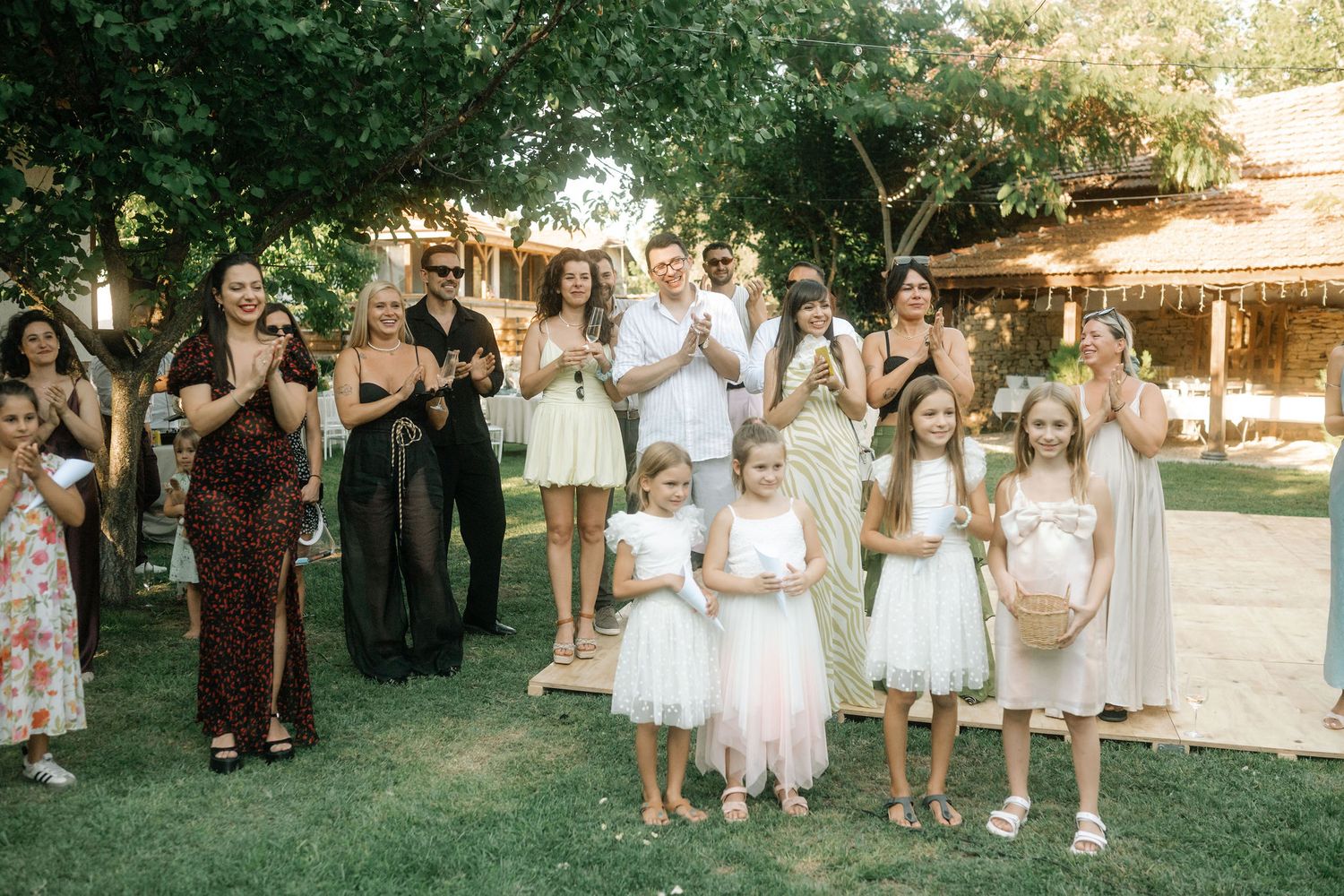 A group of wedding guests in white dresses and formal attire gather outdoors during a summer celebration.