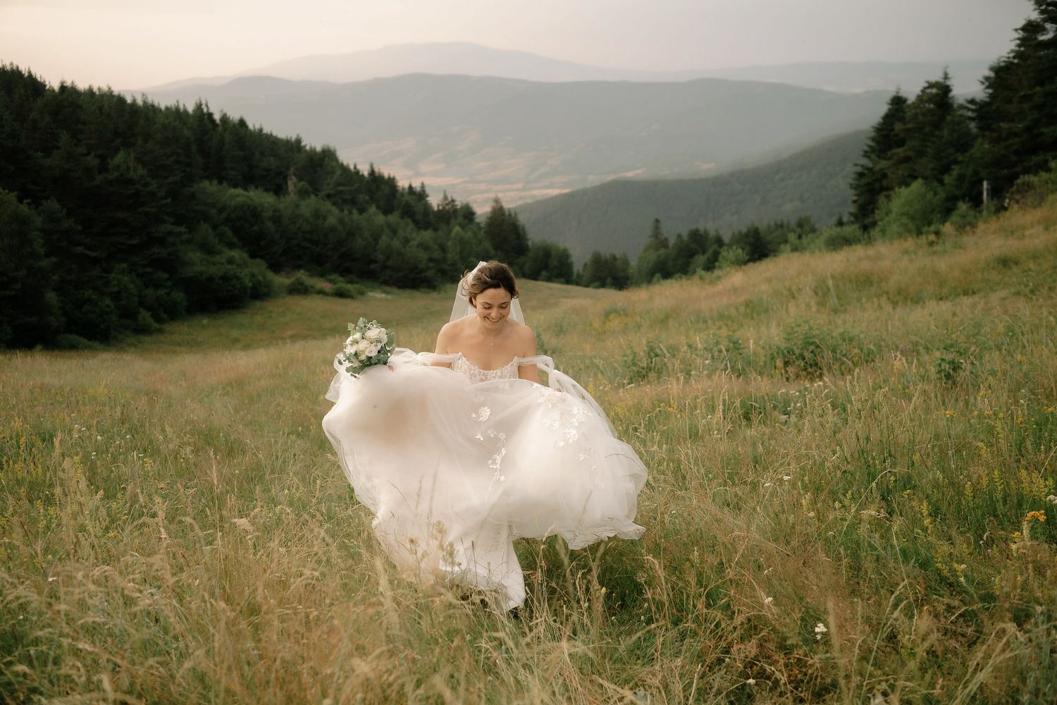 A flowing white wedding dress billows dramatically against a scenic mountain landscape at sunset.