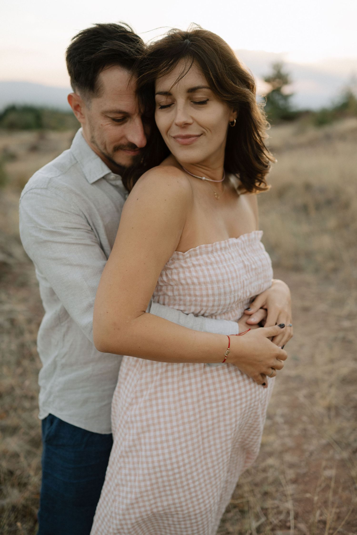 A couple embraces tenderly in a golden field at sunset wearing white and denim.