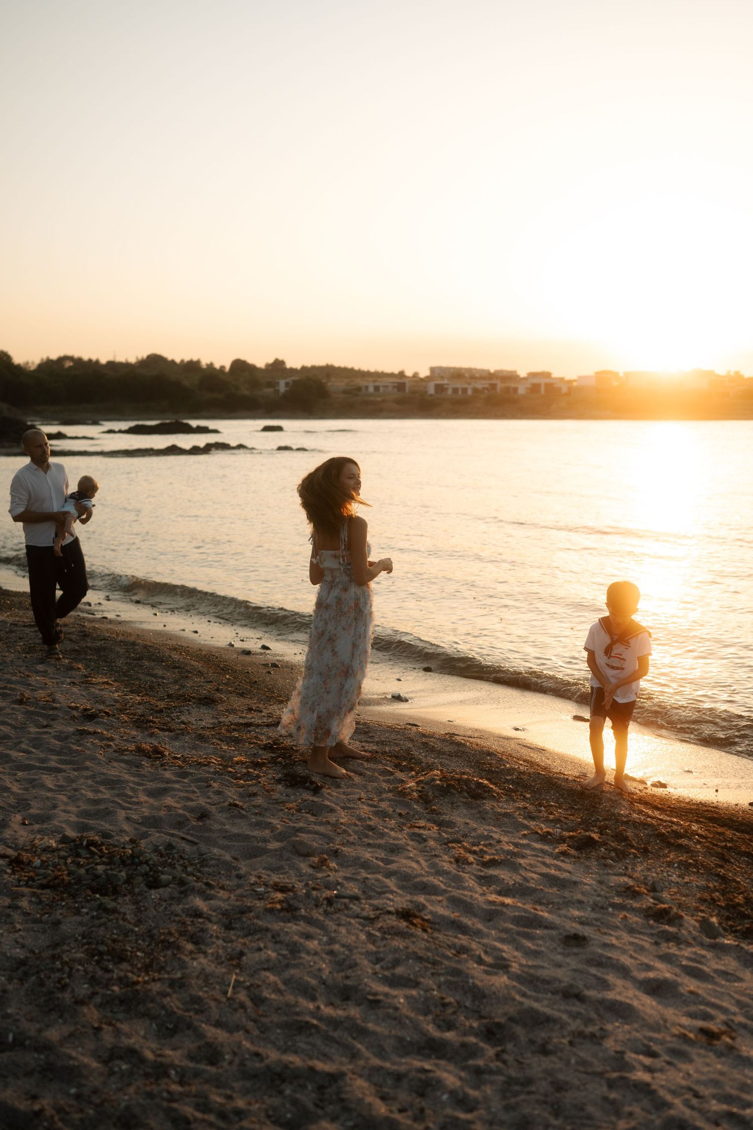 A couple embraces on a sandy beach at sunset with golden light illuminating the shoreline and ocean waves.