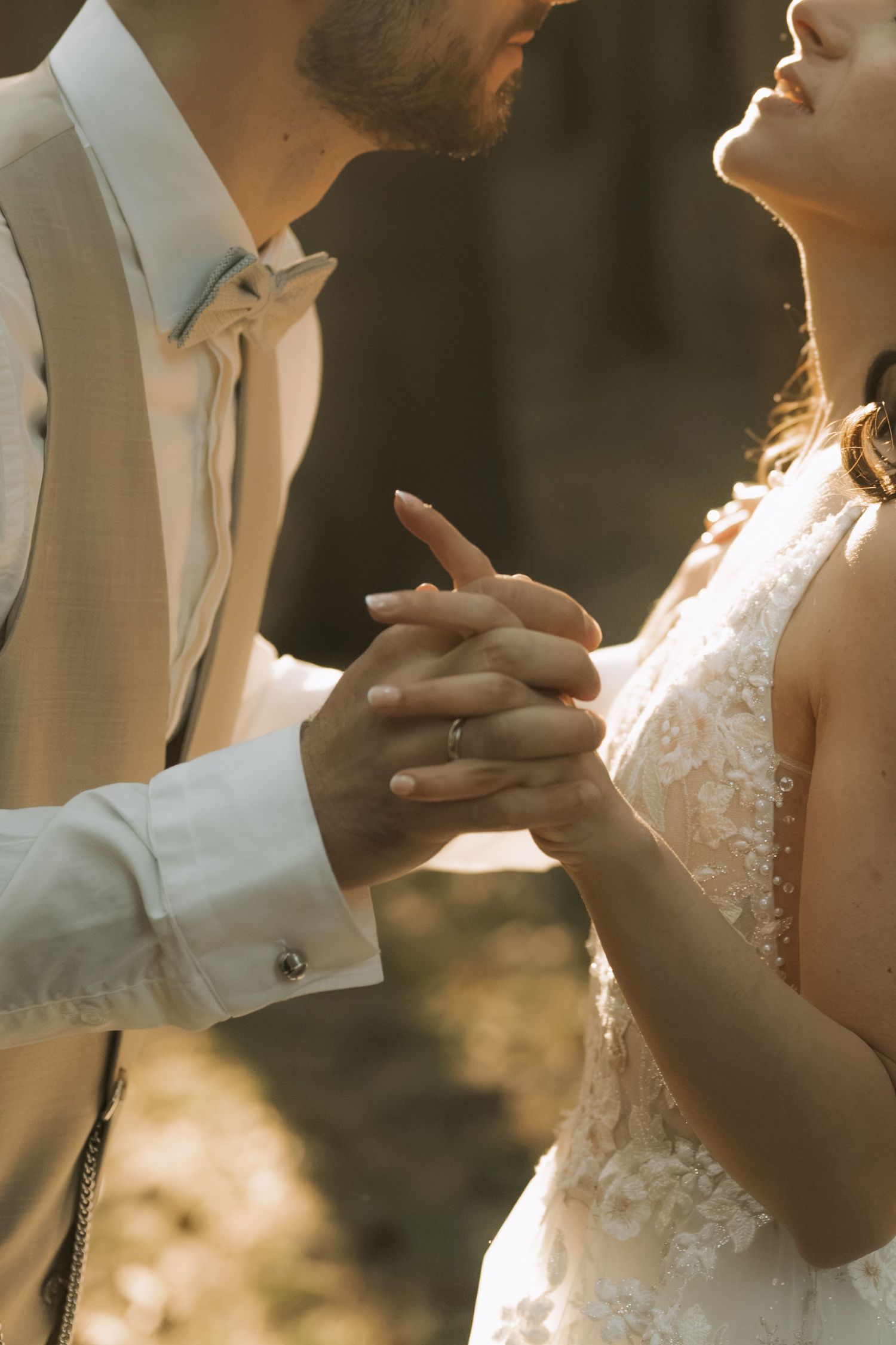 Bride and groom holding hands during wedding ceremony, wearing lace dress and beige suit.