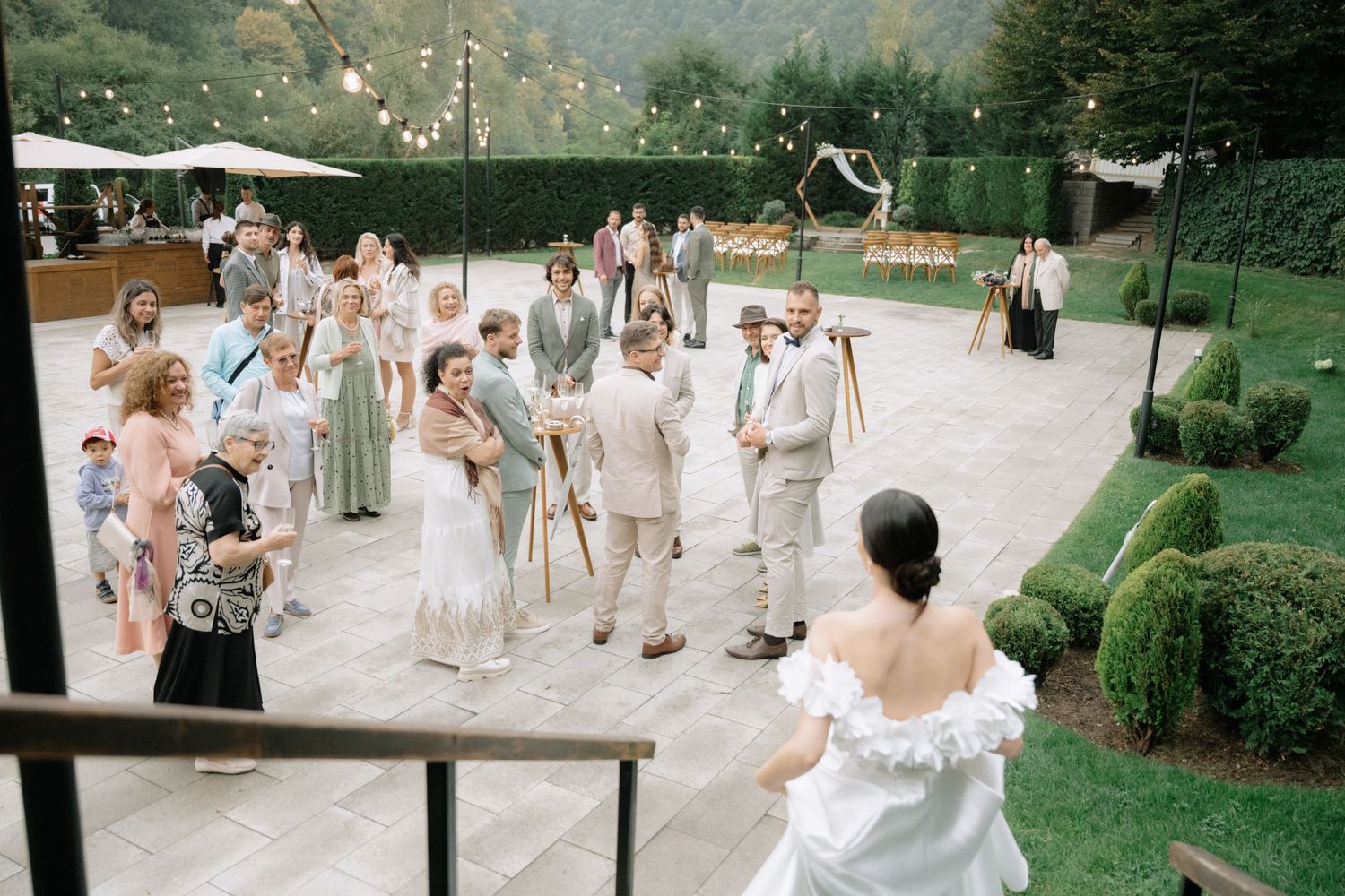 Guests blow bubbles at an outdoor wedding celebration while standing on a stone patio surrounded by greenery.