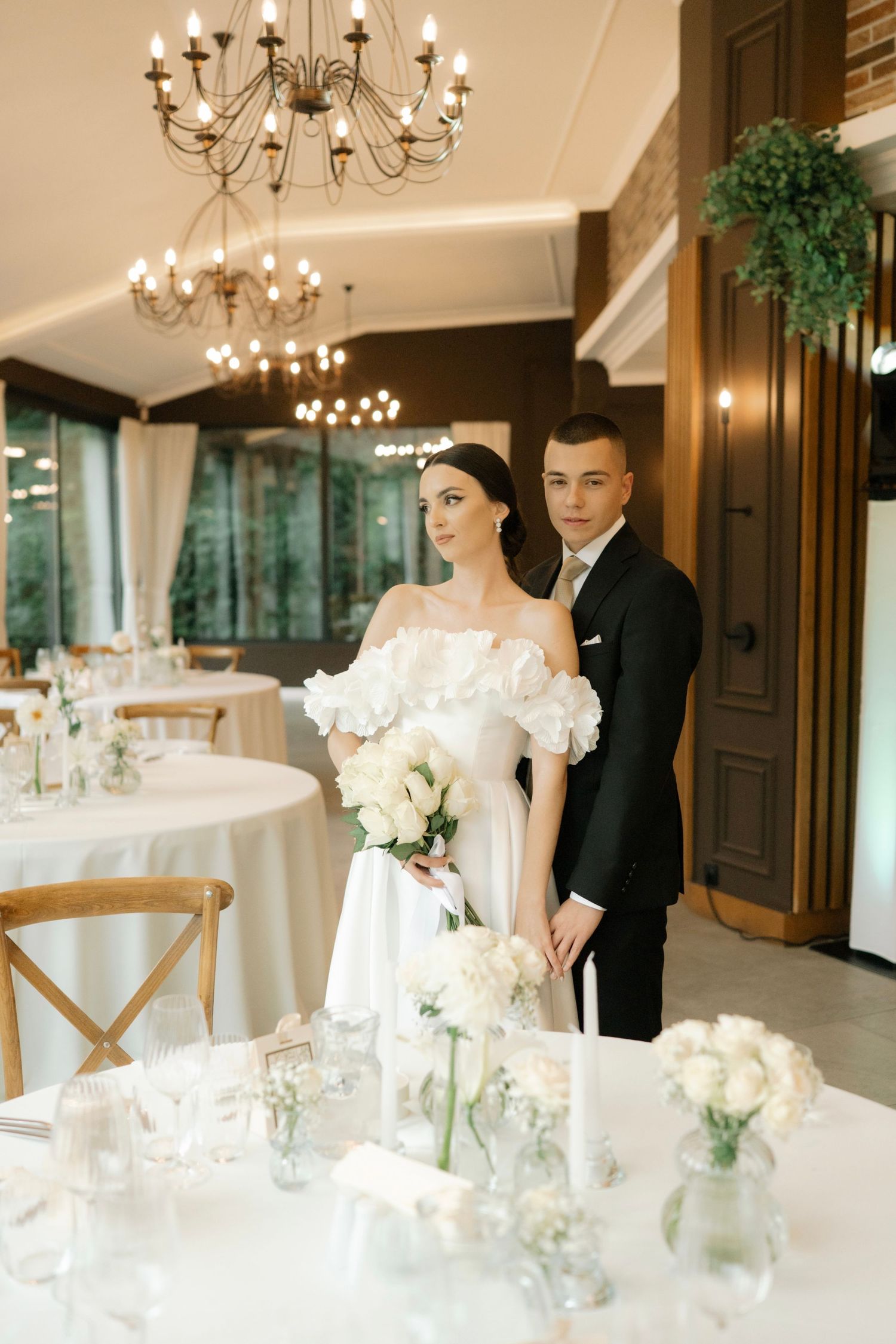Elegant wedding reception venue with white floral centerpieces, chandeliers, and romantic table settings in a luxurious ballroom.