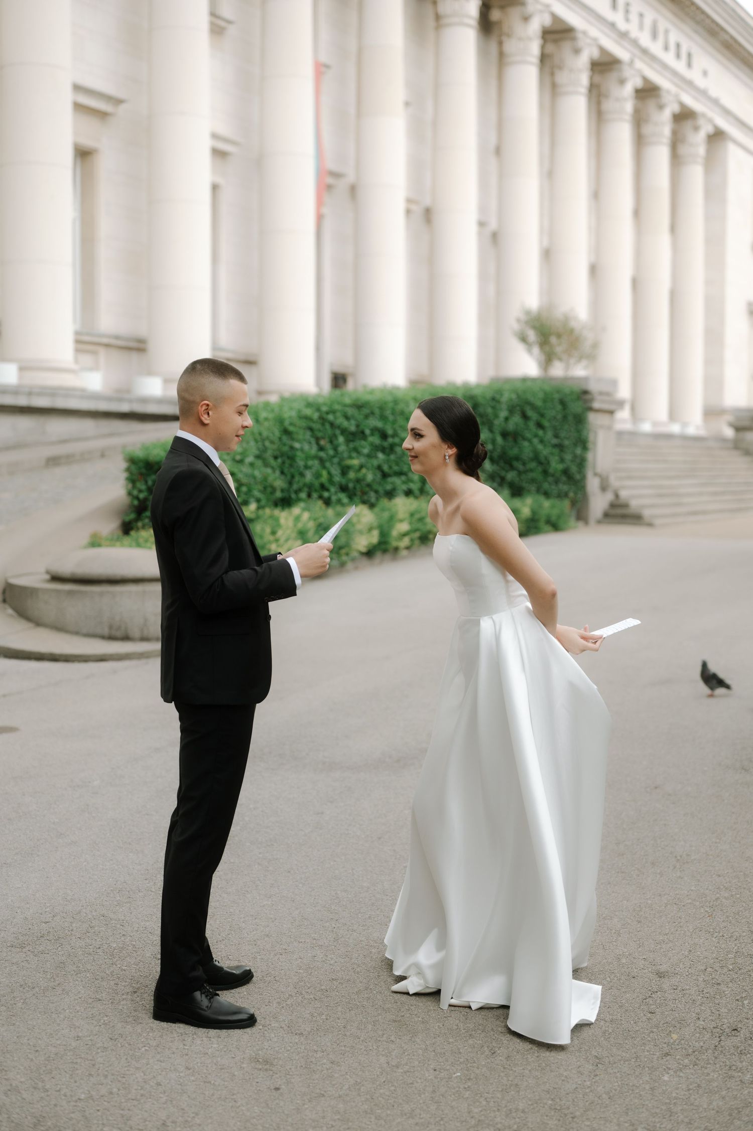 A couple shares a joyful moment during their first look on their wedding day outside a grand columned building.