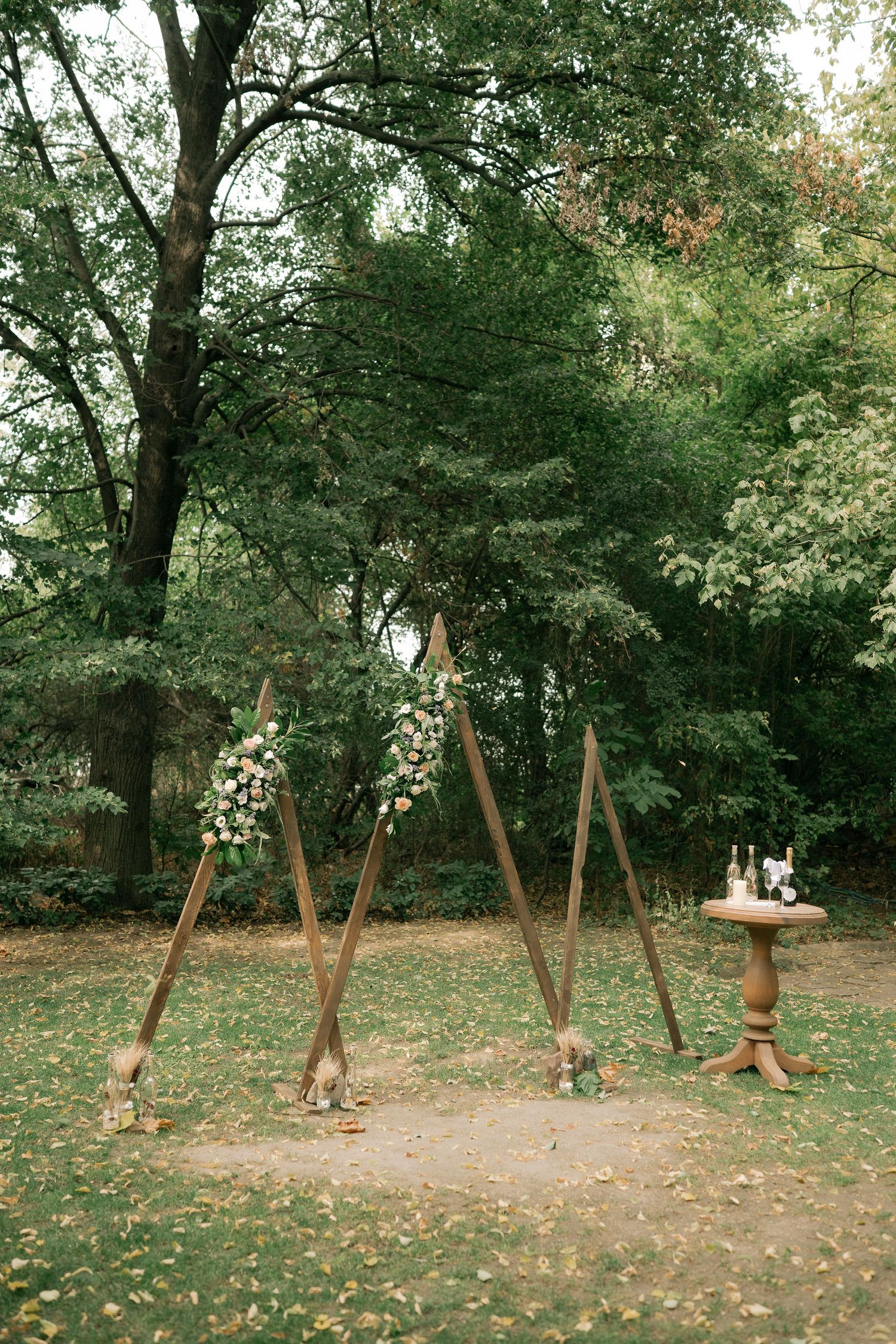 Rustic wooden swing set with multiple swings stands in a peaceful wooded park setting surrounded by autumn leaves.