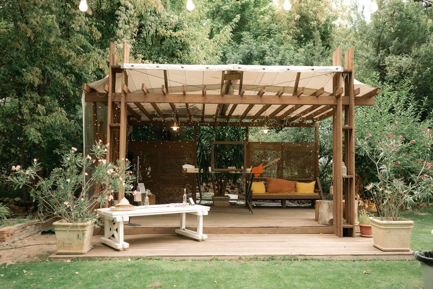 A wooden pergola structure with string lights creates an inviting outdoor seating area in a garden setting.