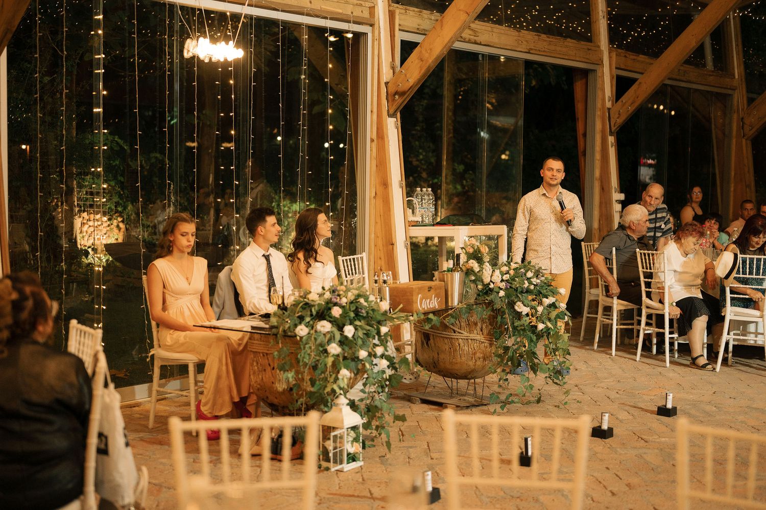 Wedding guests dance and celebrate inside a rustic barn venue decorated with twinkling lights and floral arrangements.