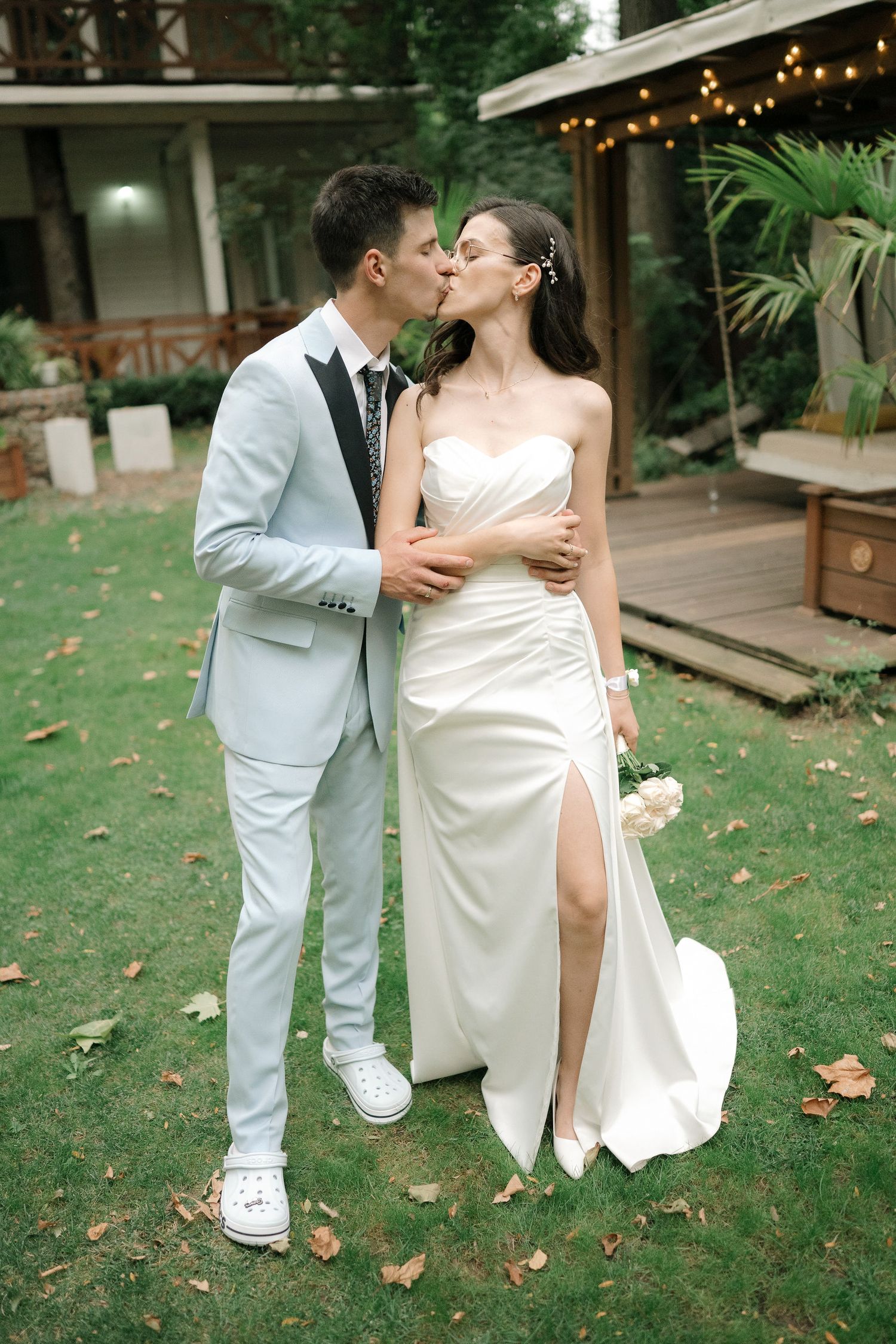 Romantic wedding couple shares intimate moments in a garden setting with string lights and greenery.