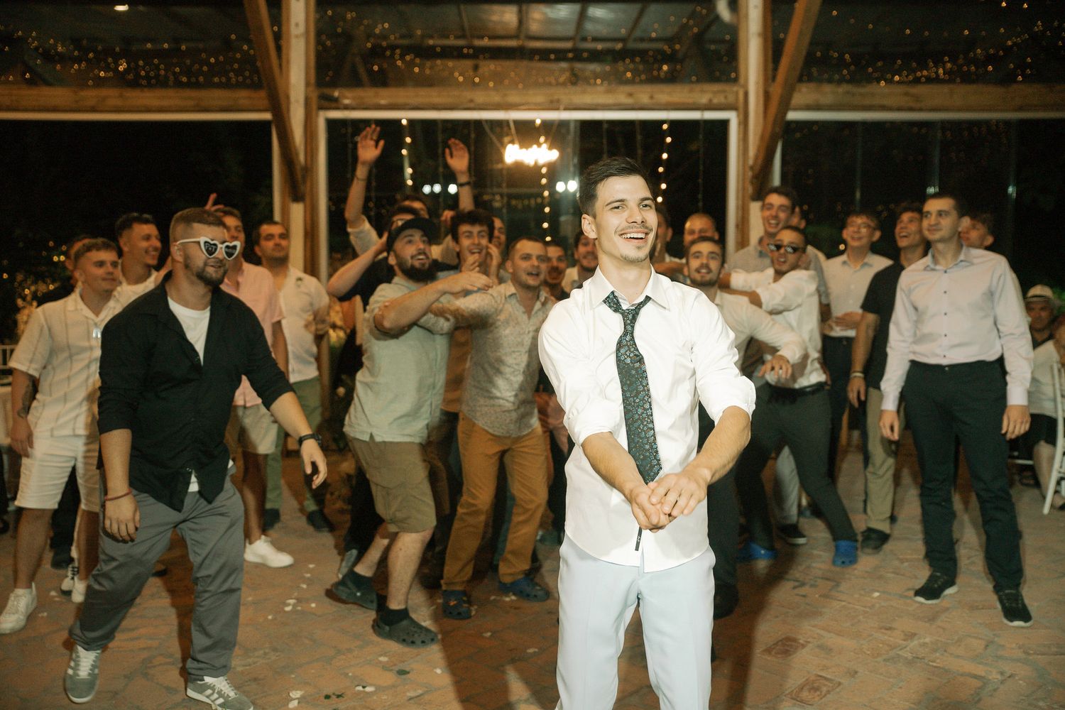 Energetic crowd dancing and celebrating at a barn wedding reception with twinkle lights decorating the ceiling.