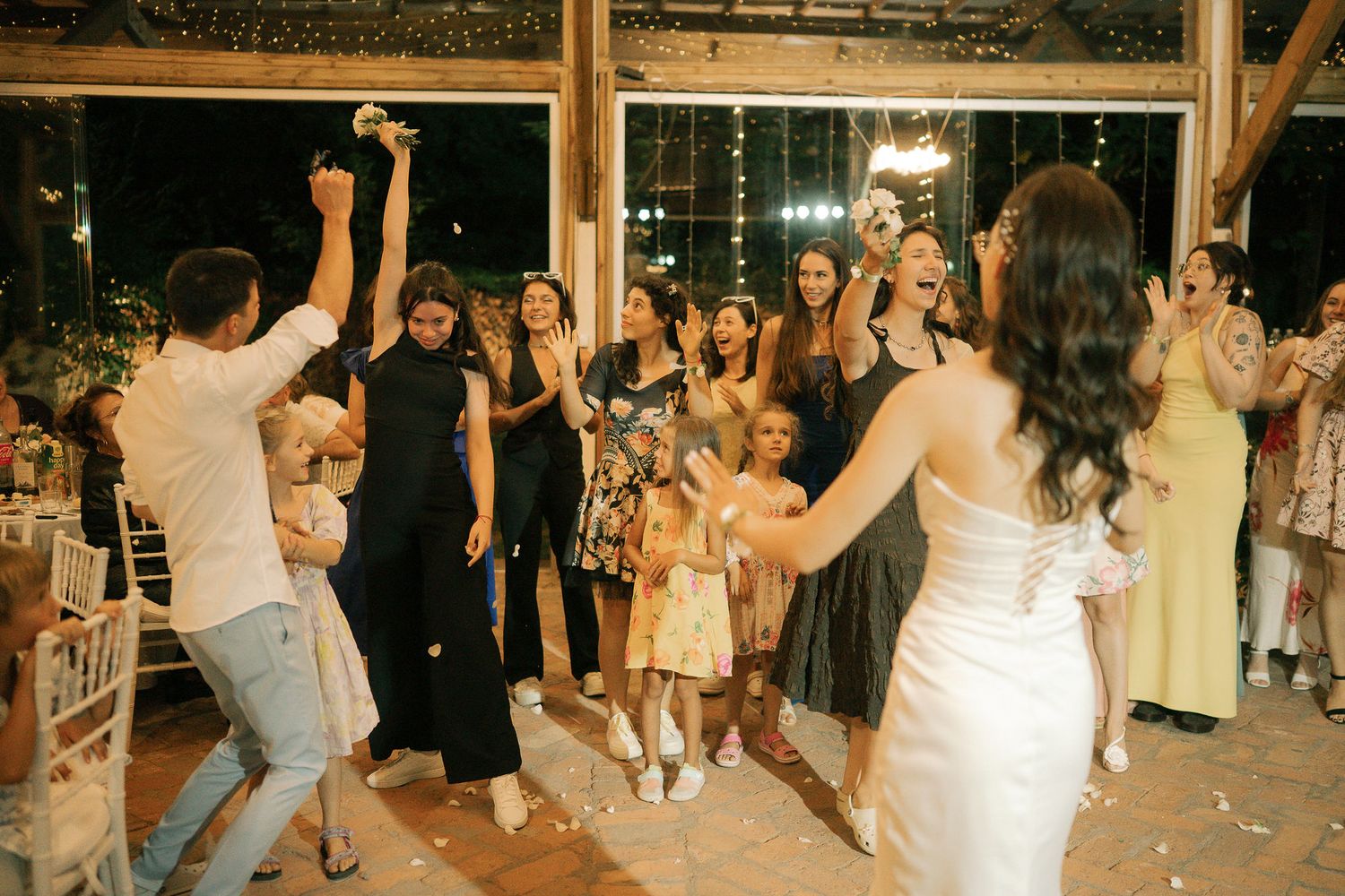Wedding guests dancing and celebrating together on a rustic wooden dance floor at an indoor reception venue.