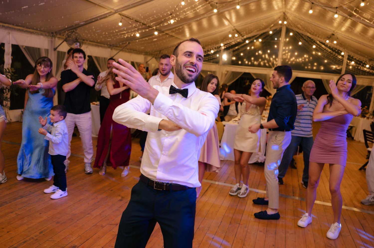 People dancing together in a large indoor venue with string lights hanging from the ceiling during a celebration.