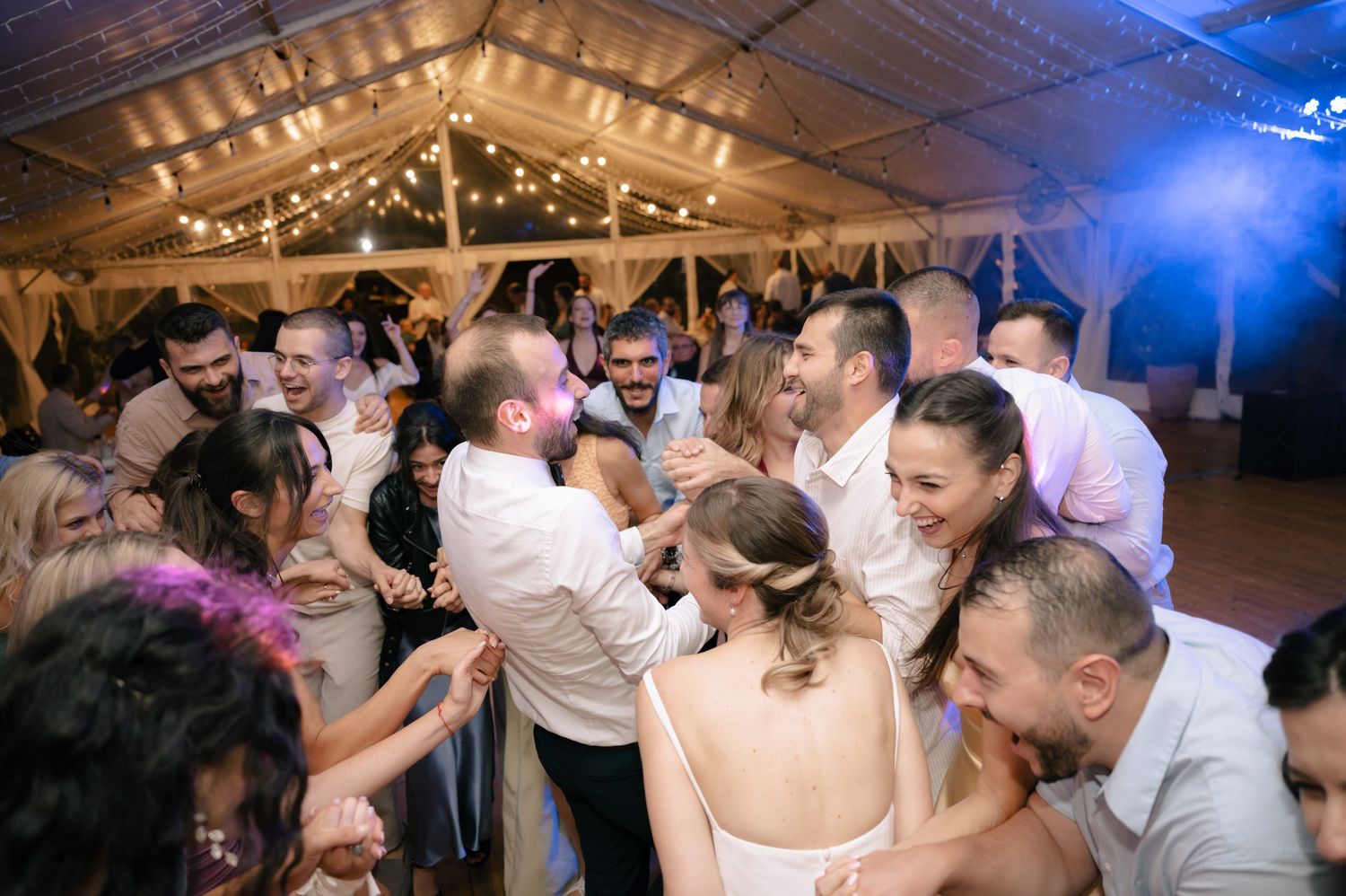 Wedding reception guests dancing together under twinkling lights at an evening celebration.