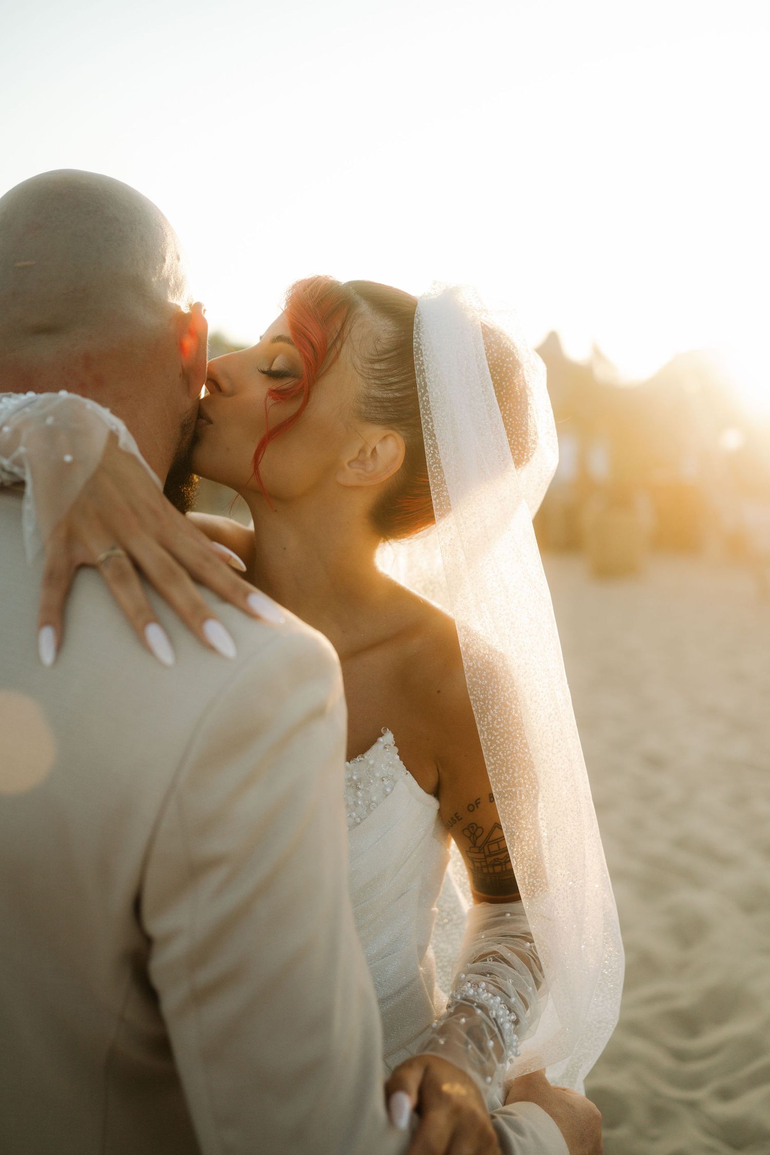 Romantic sunset beach wedding moment captured as newlyweds share an intimate kiss in golden sunlight.