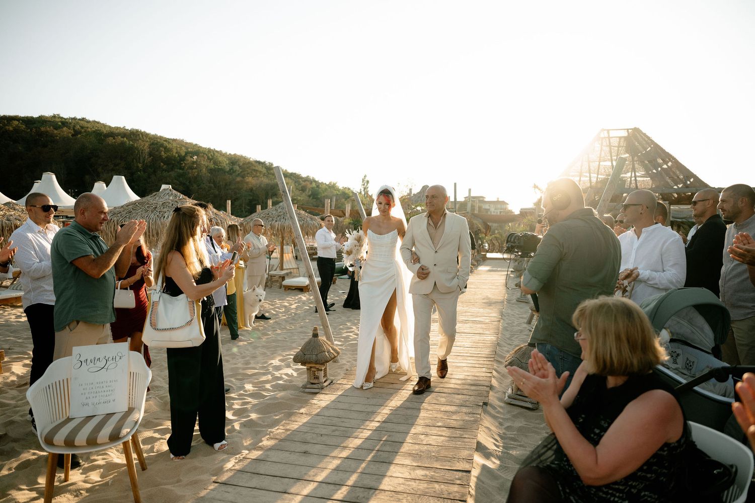 A series of wedding guests dancing outdoors at sunset on a paved terrace with mountains in the background.